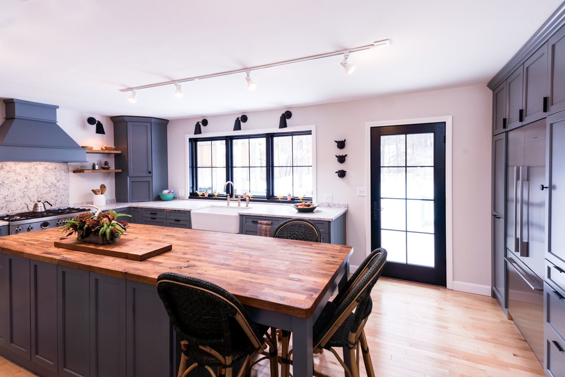 Modern kitchen with large wooden island, black chairs, gray cabinets, and bright windows