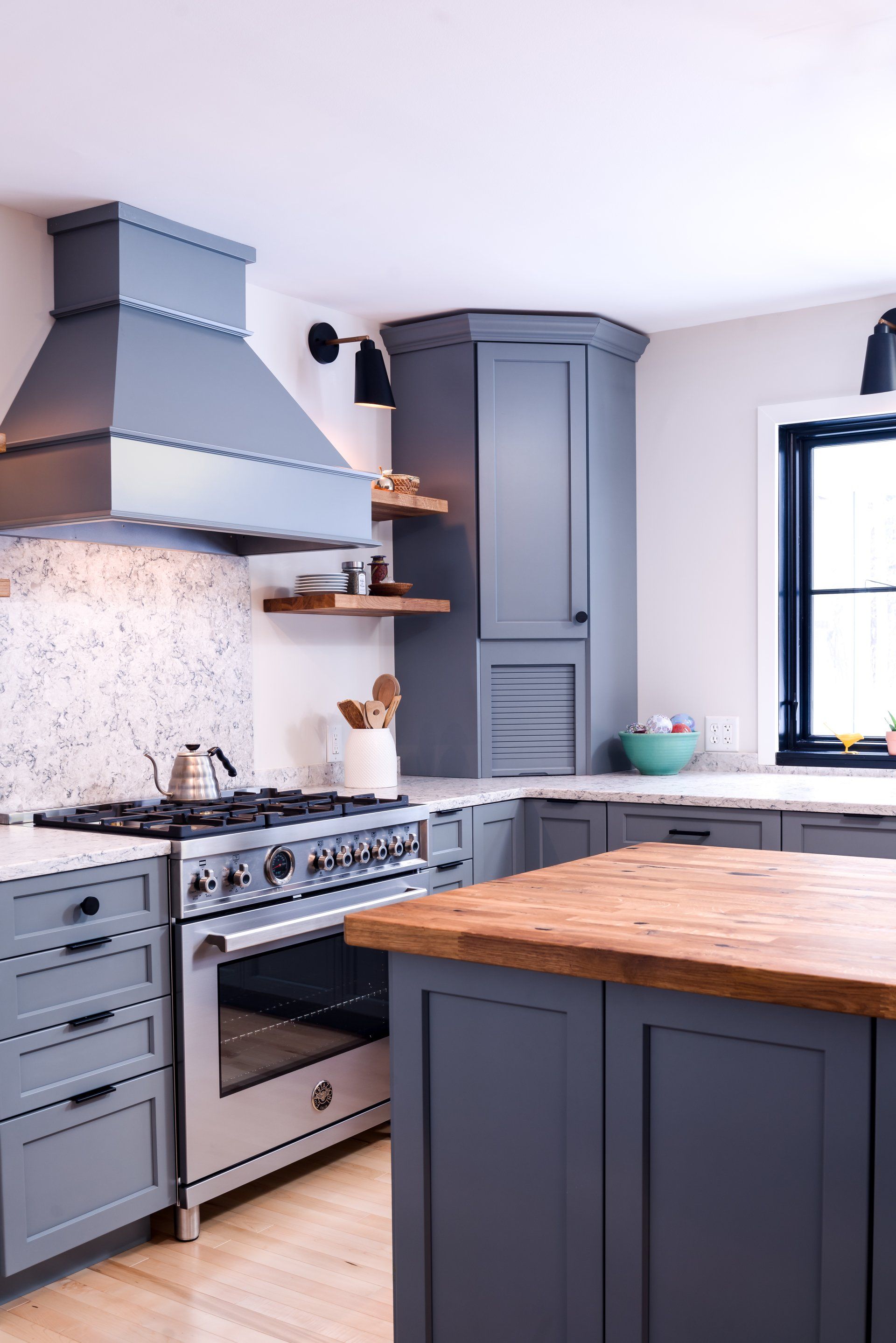 Modern gray kitchen with stainless steel range, wooden island, and window light
