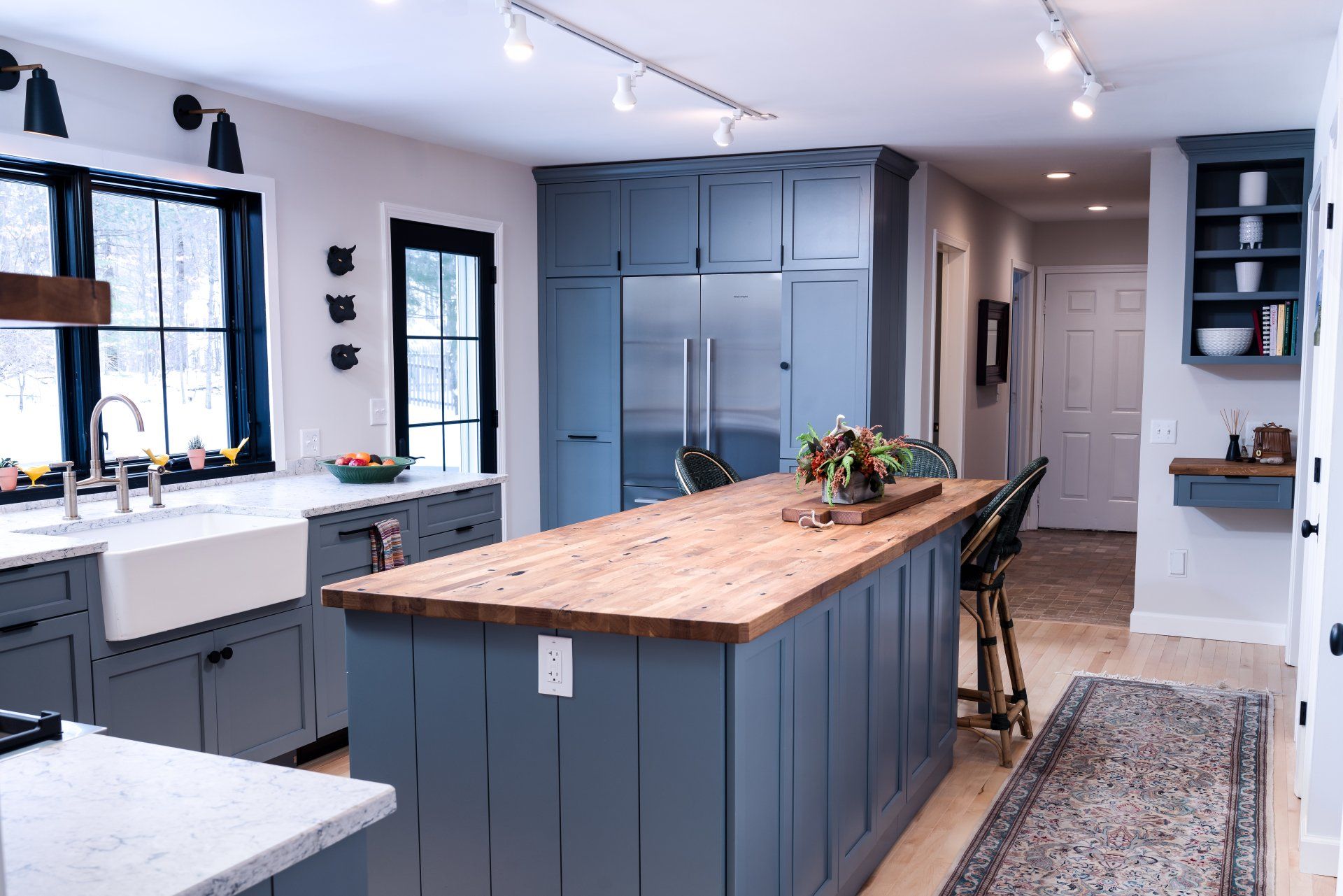 Bright kitchen with blue cabinets, a large wooden island, and black-framed windows.