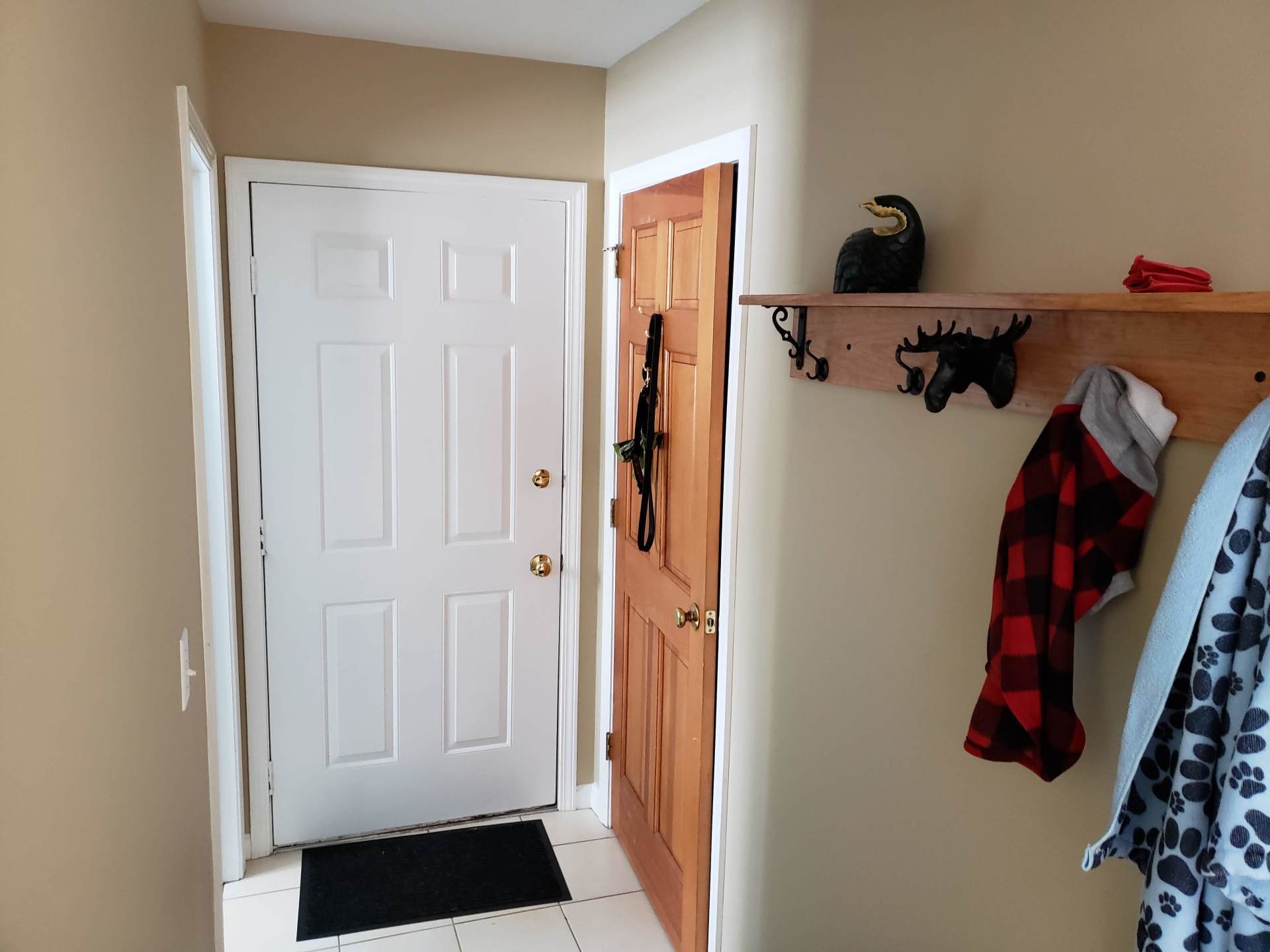 Front entryway with white door, wooden coat rack, and a black doormat on beige walls.