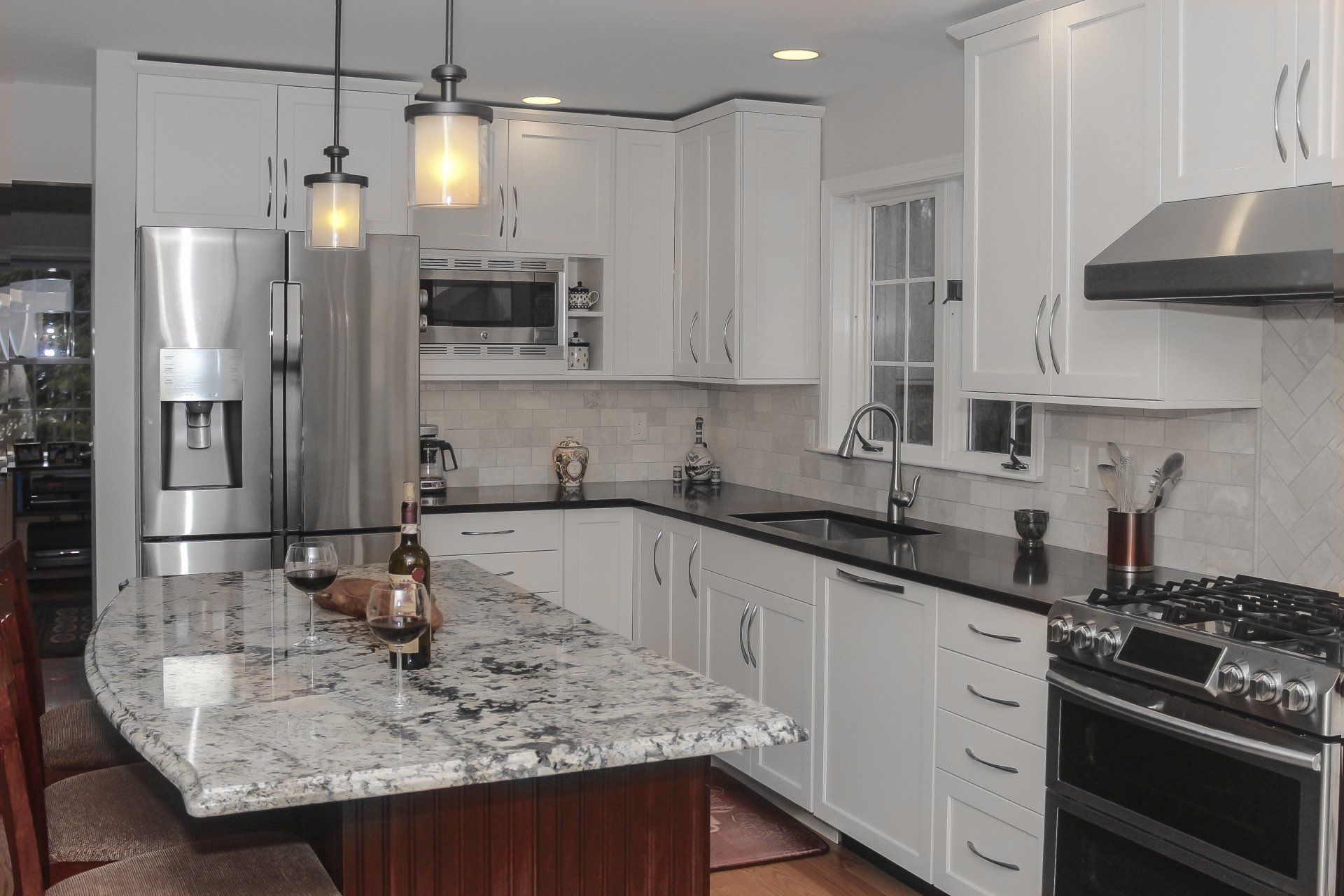 Modern kitchen with white cabinets, granite island, stainless steel appliances, and pendant lighting