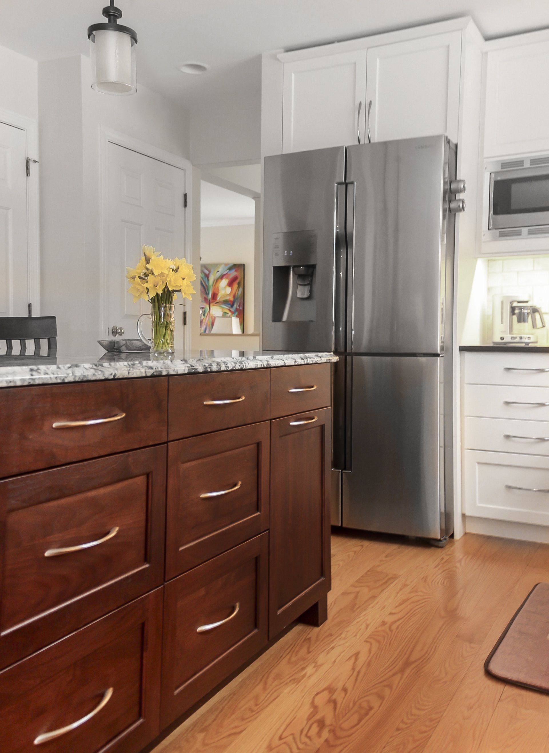 Bright kitchen with dark wood island, stainless steel fridge, white cabinets, and yellow flowers on the counter.