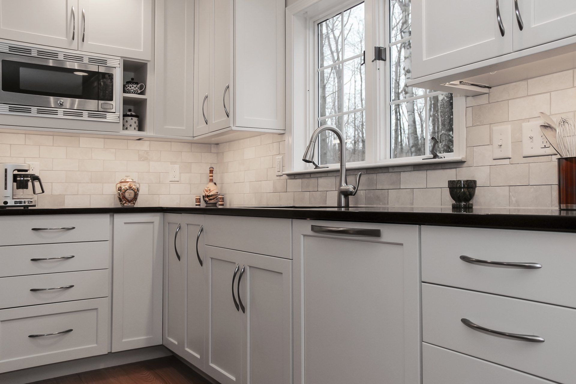 Bright modern kitchen with white cabinets, black countertop, stainless appliances, and a window over the sink