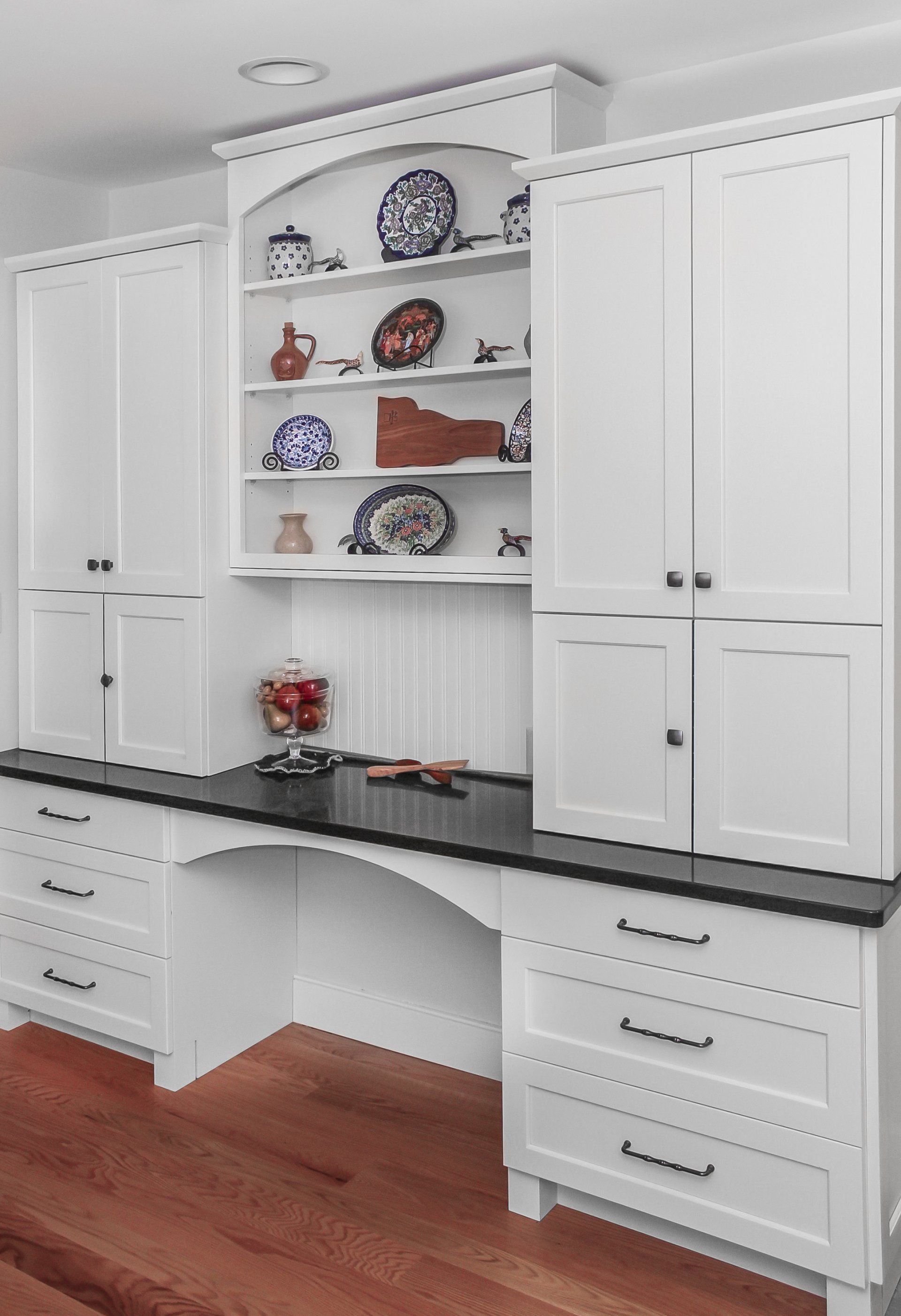 White built-in desk and cabinets with black countertop and open shelves in a home office.