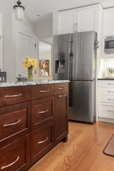 Kitchen with stainless steel fridge, dark wood island, and white cabinets, with yellow flowers on the counter