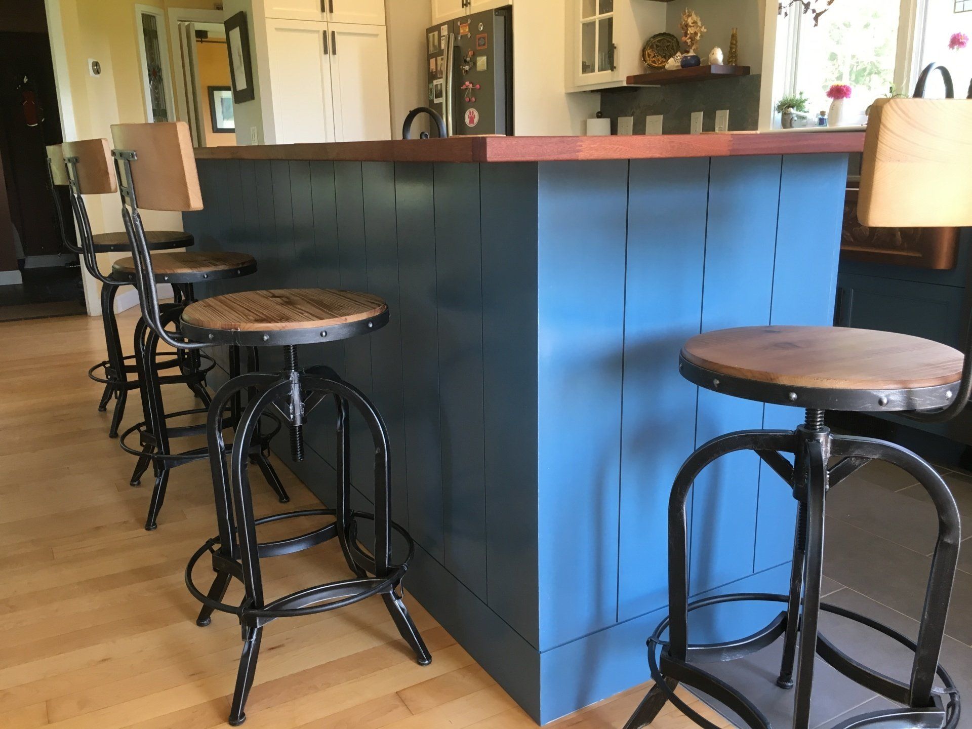 Cozy bar area with blue counter, wooden top, and tall stools in a bright kitchen-living space
