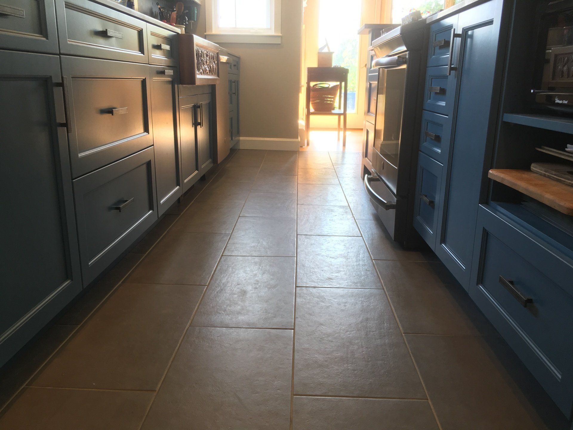 Kitchen floor between dark cabinets, with sunlight streaming in from a window at the far end.