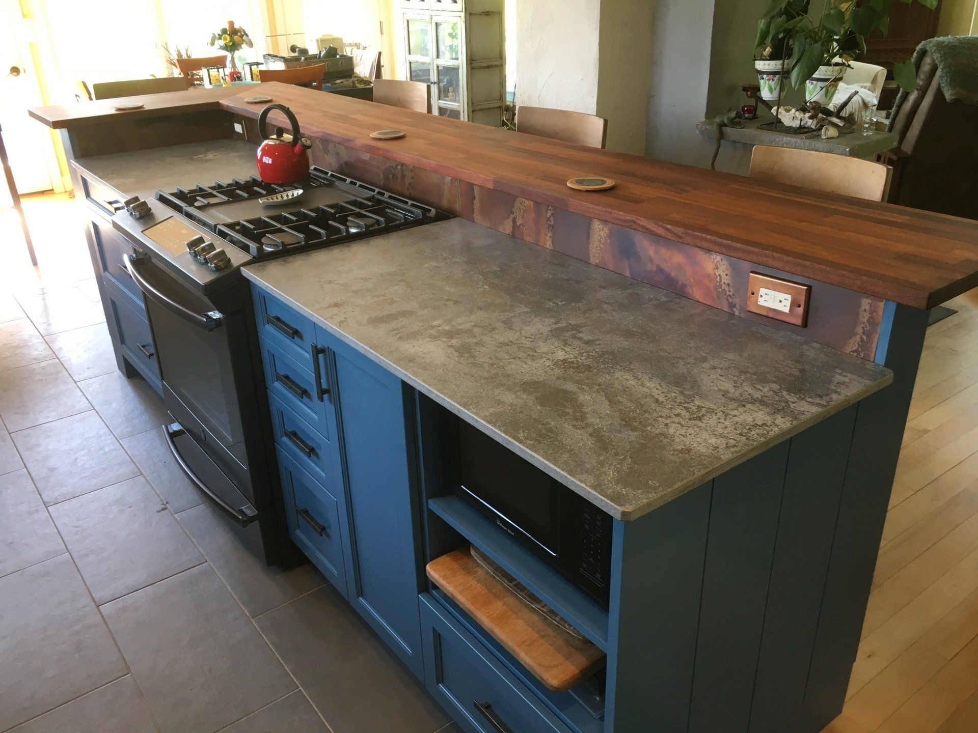 Modern kitchen island with blue cabinets, gray countertop, wooden breakfast bar, and gas stove