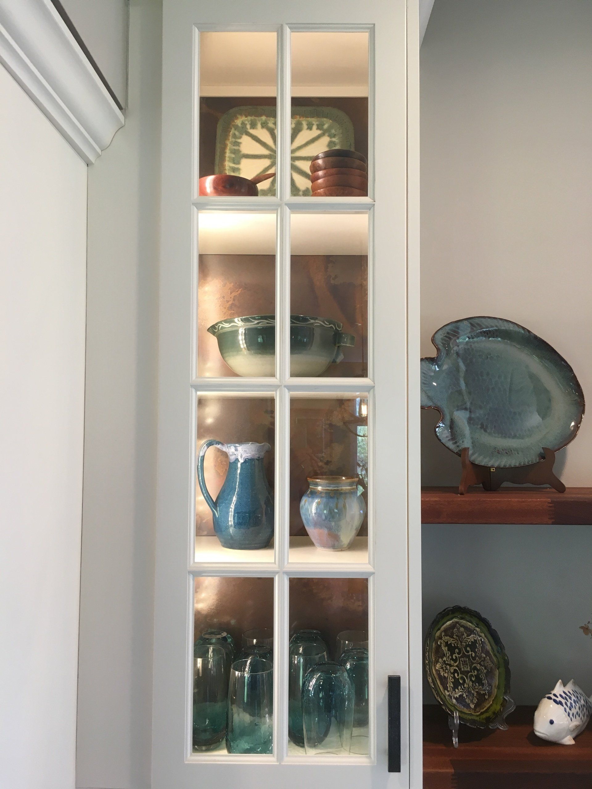 Glass-front cabinet displaying blue glassware and decorative dishes in a home interior.