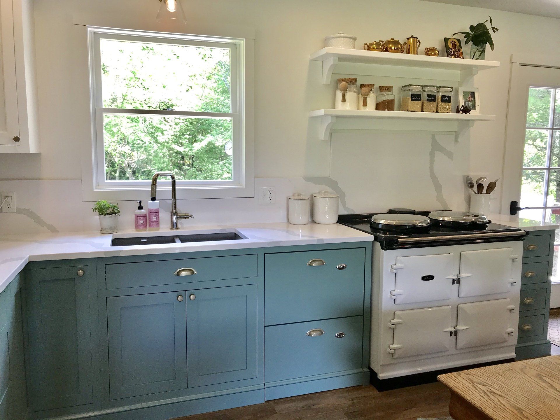 Bright kitchen with blue lower cabinets, white countertops, a farmhouse sink, and a white stove.