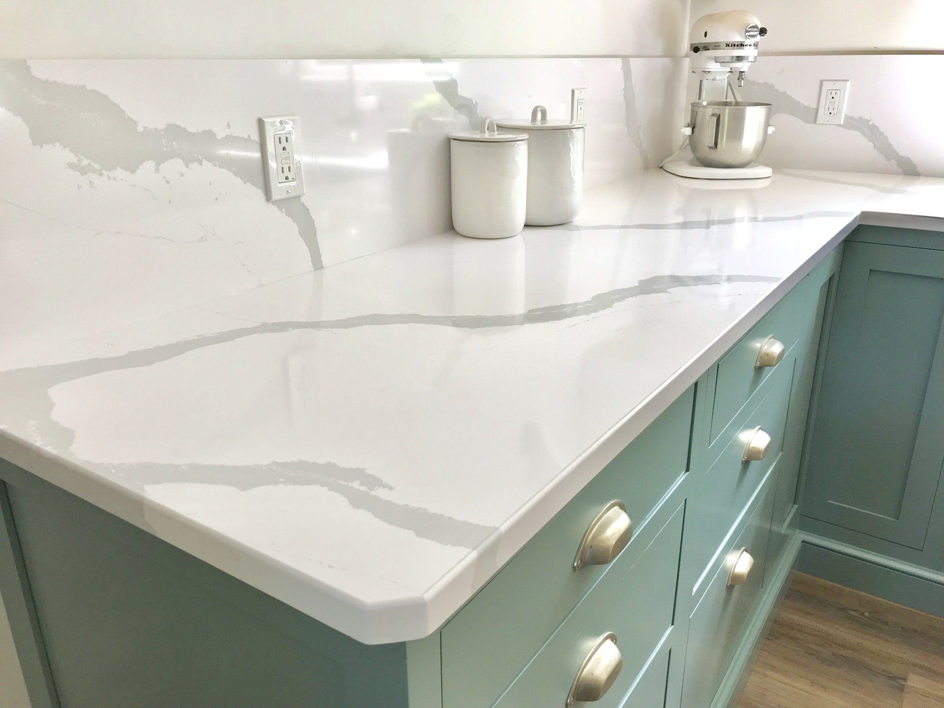 White marble kitchen countertop with gray veining above teal cabinets and gold handles