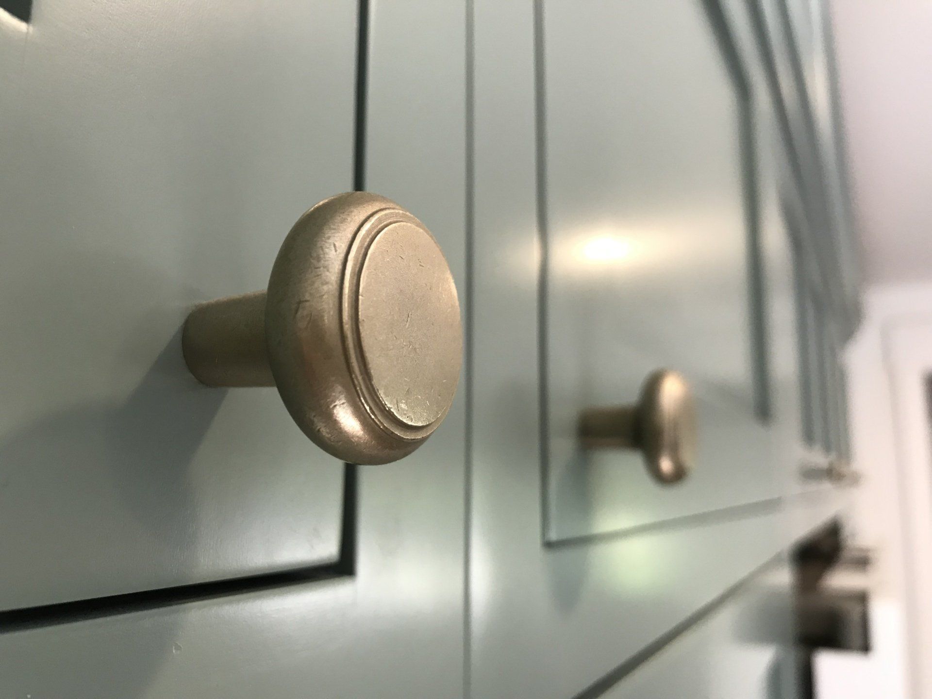 Close-up of light gray cabinet drawers with round metal knobs, one in sharp focus and one blurred in the background