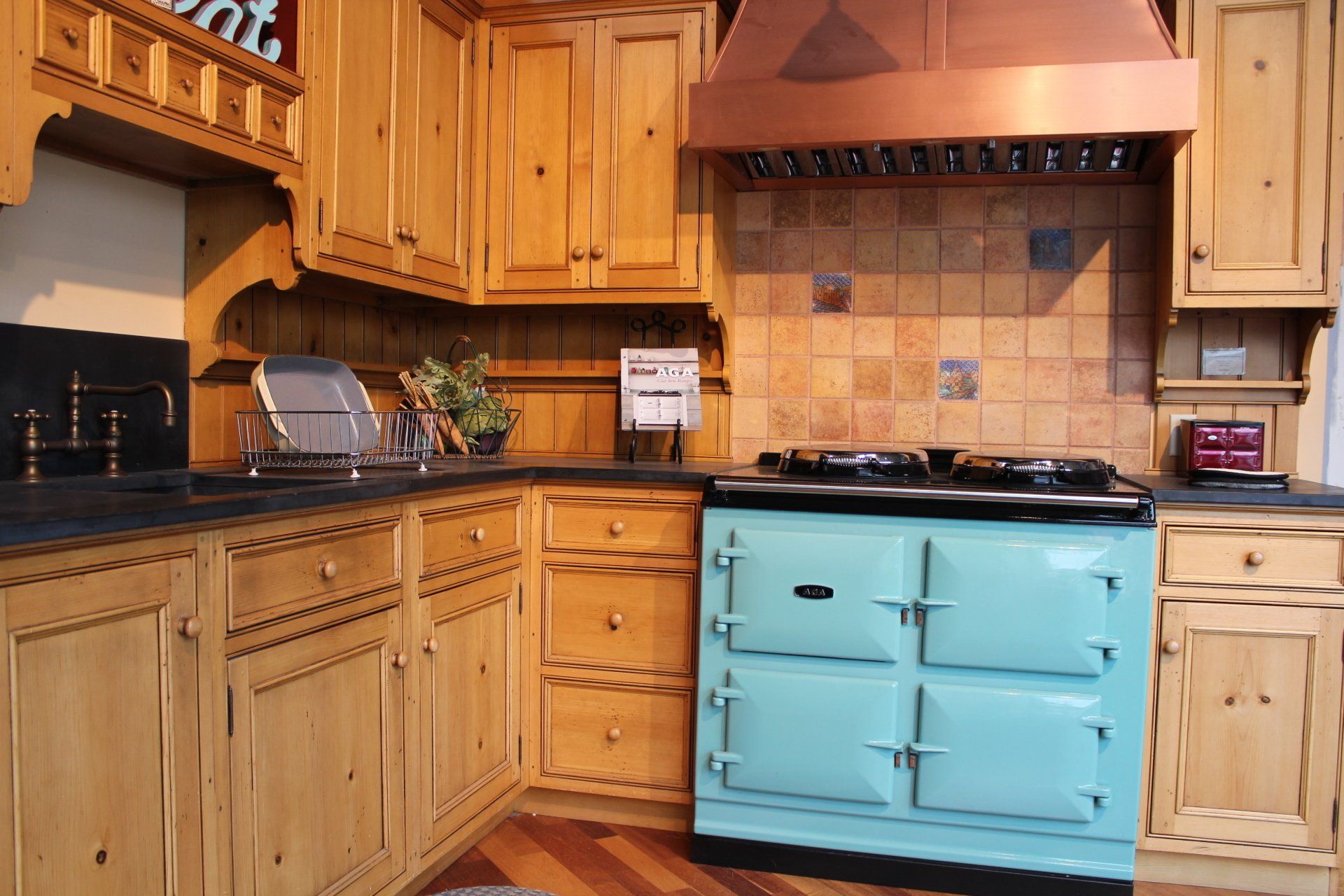 Wooden kitchen with turquoise stove and cabinets, tiled backsplash, and copper range hood