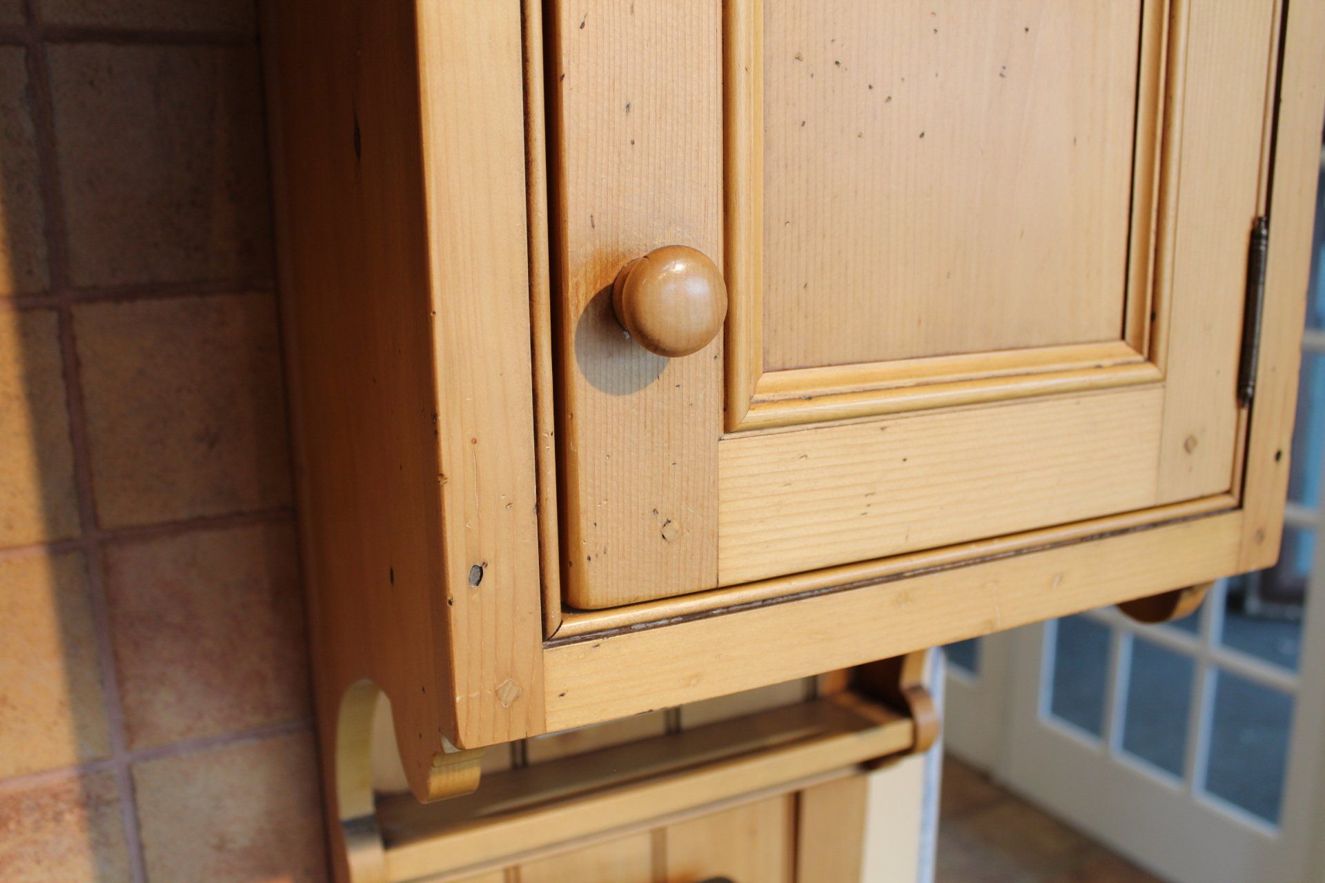 Close-up of a light wood cabinet door with a round knob, showing chipped paint near the hinge.