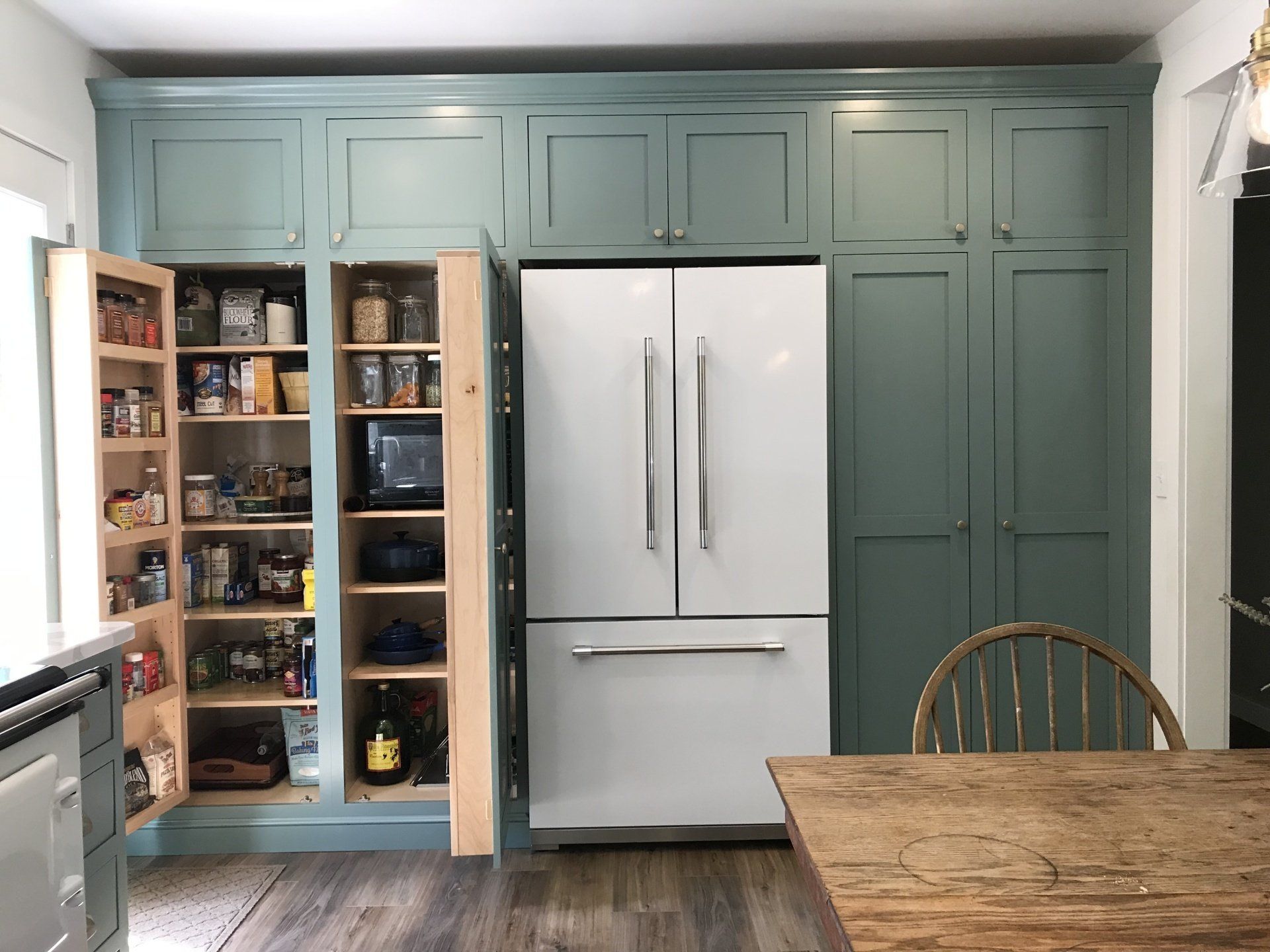 Kitchen with open pantry cabinets beside a white refrigerator and a wooden dining table