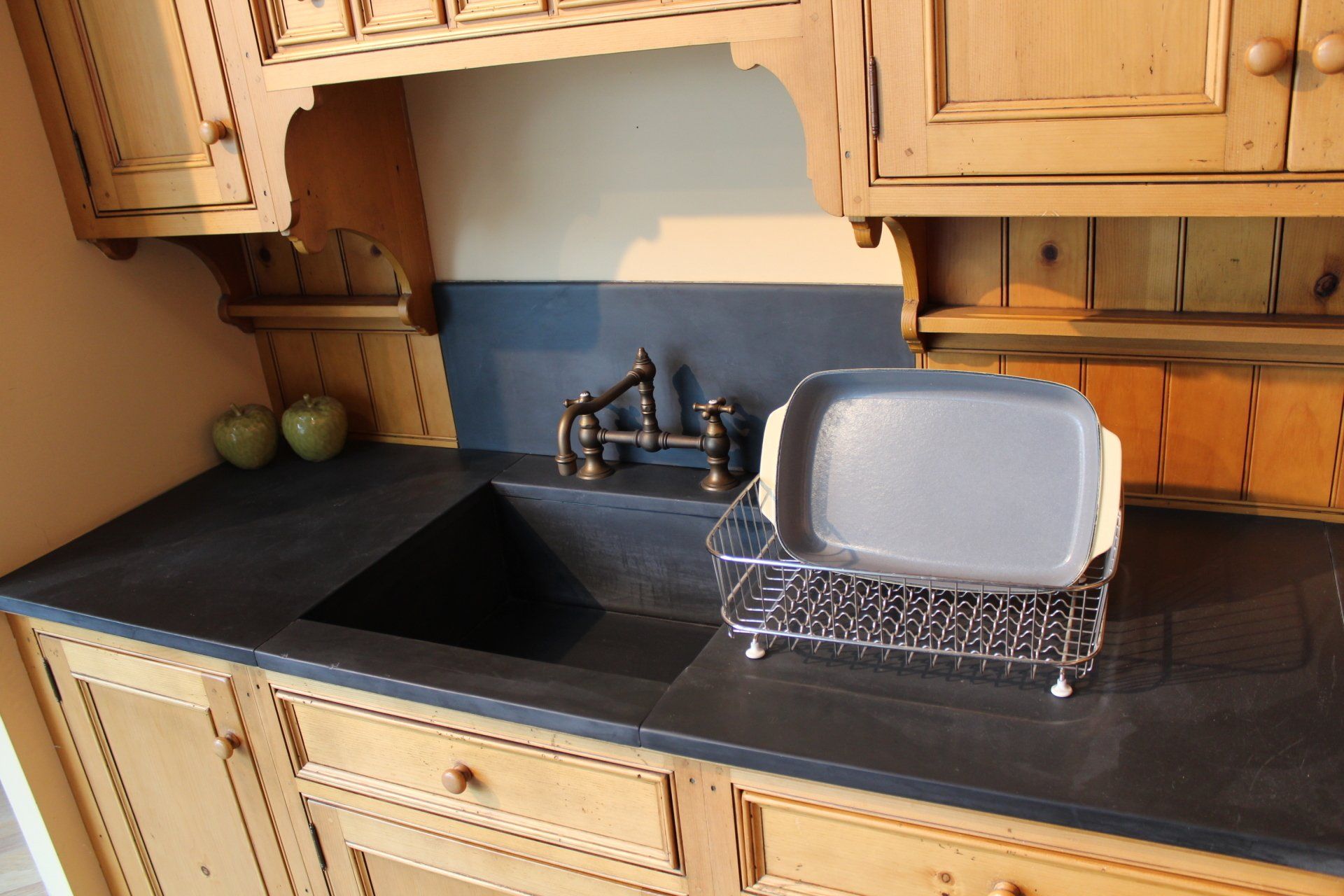 Kitchen countertop with black sink, faucet, dish rack, and light wood cabinets