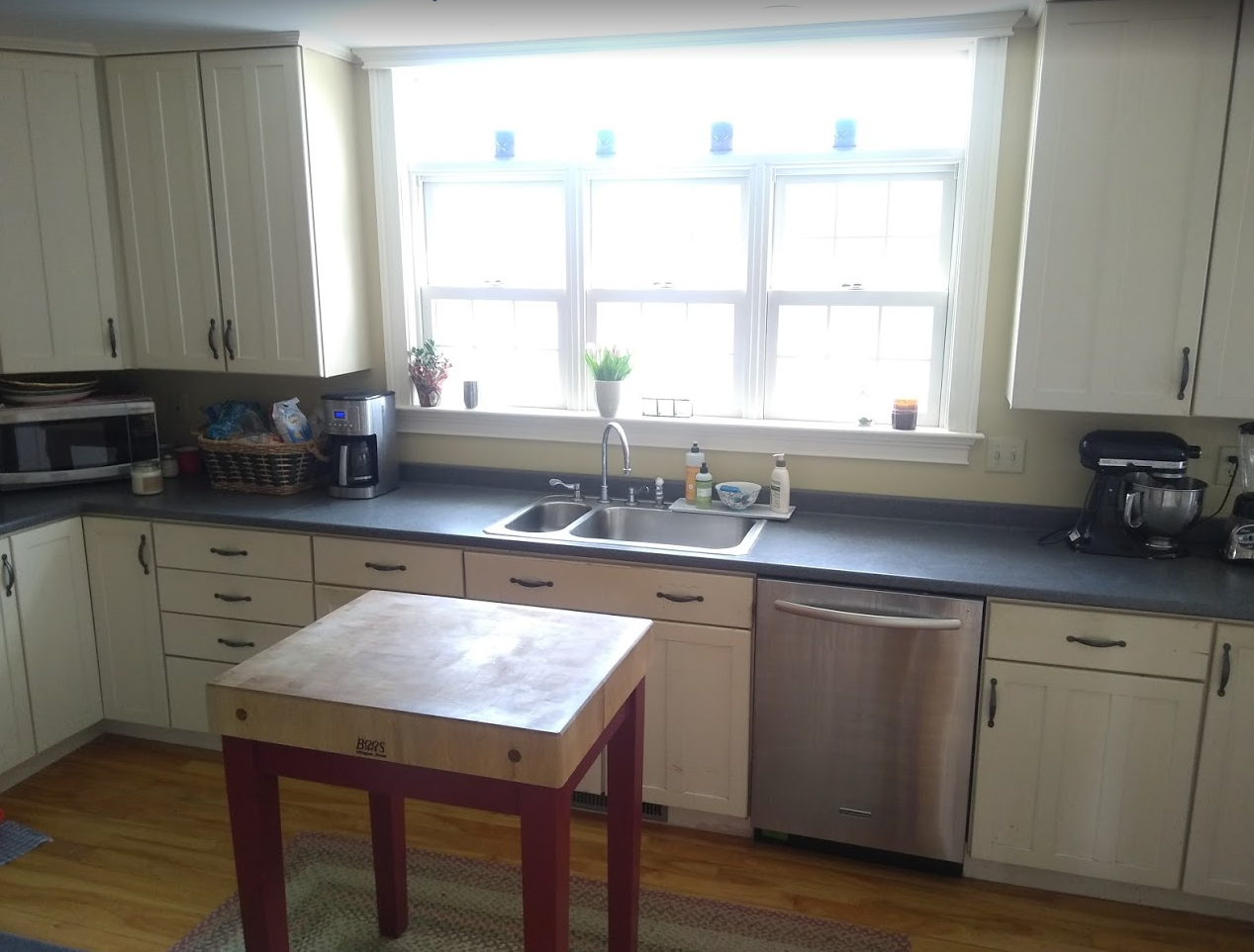 Bright kitchen with white cabinets, a large window over the sink, and a small wooden table in the center.