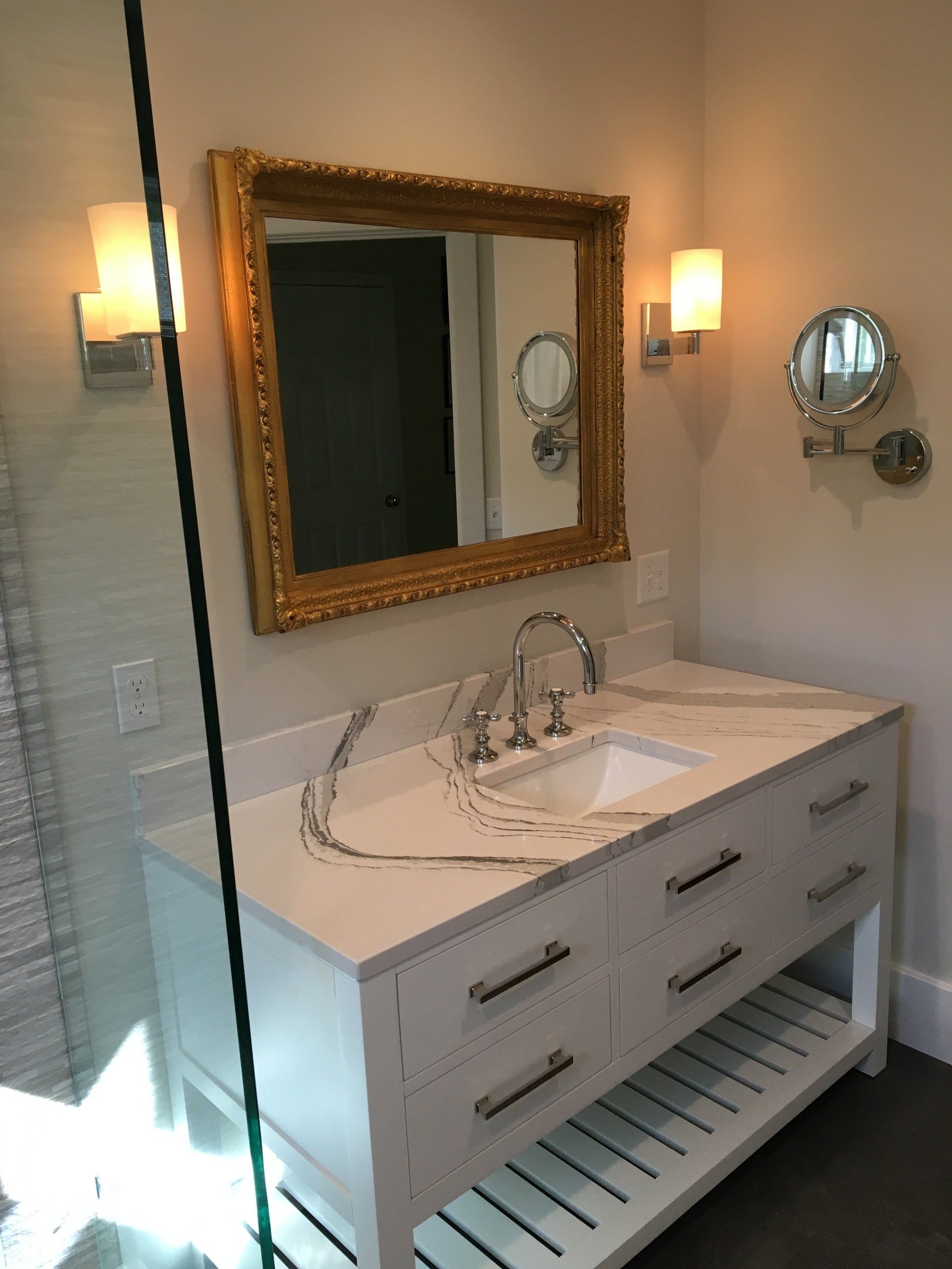 Bathroom vanity with white sink, ornate mirror, wall sconces, and striped floor tile.