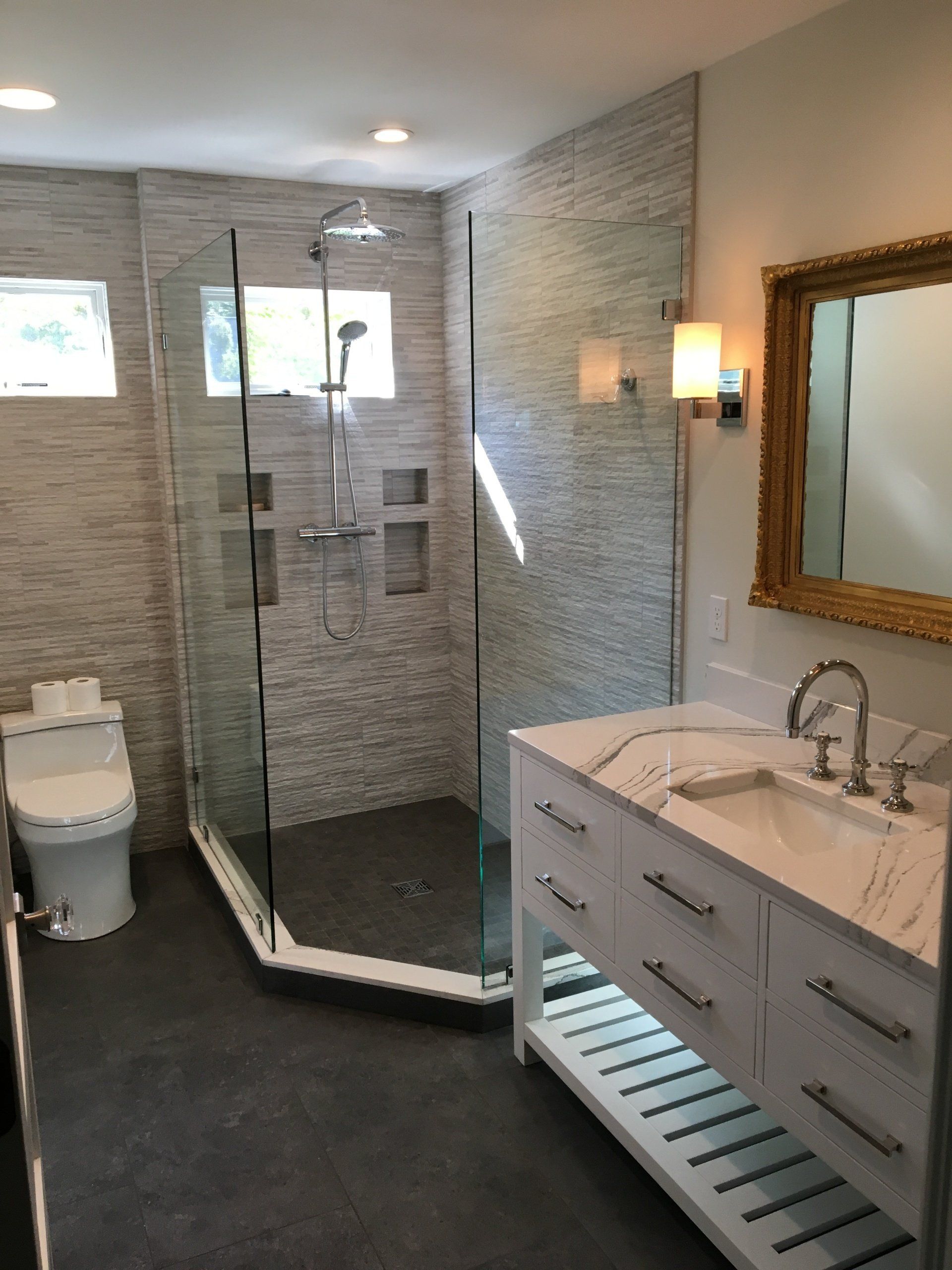 Modern bathroom with glass shower, toilet, vanity, and mirror in gray tones