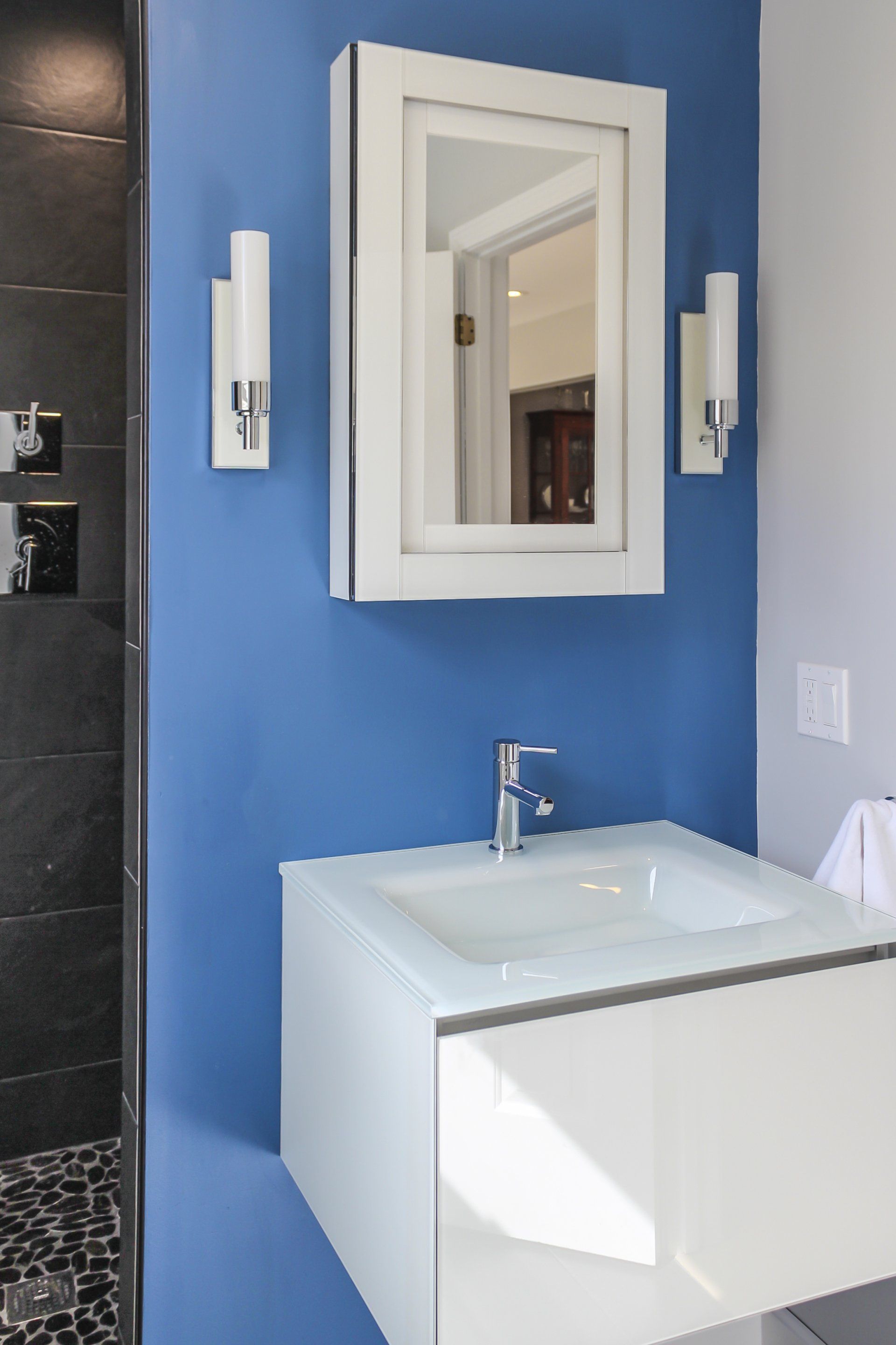 Modern bathroom vanity with white sink, mirror cabinet, and wall sconces against a blue wall
