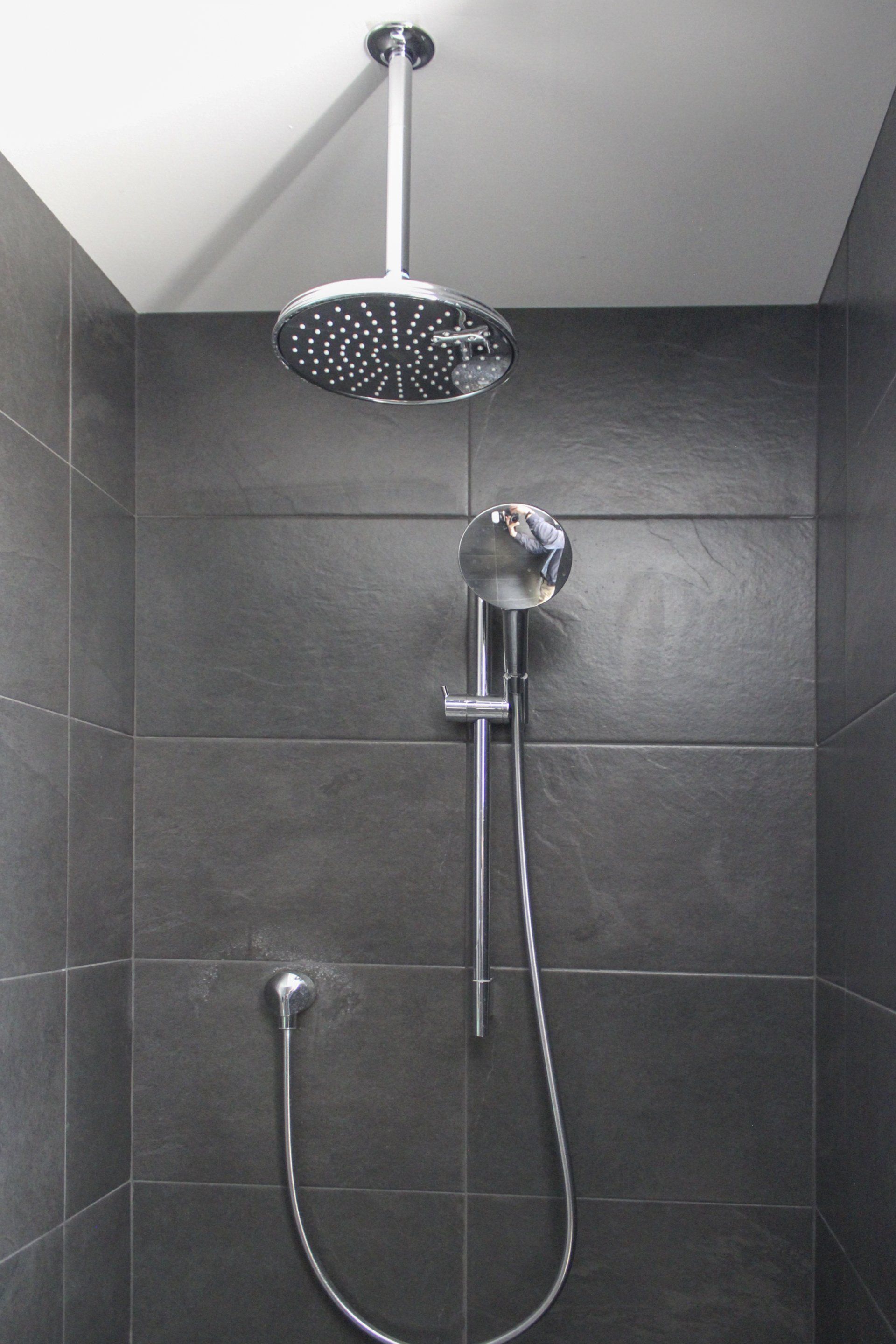 Accessible shower with handheld sprayer and overhead rain showerhead in a tiled bathroom.