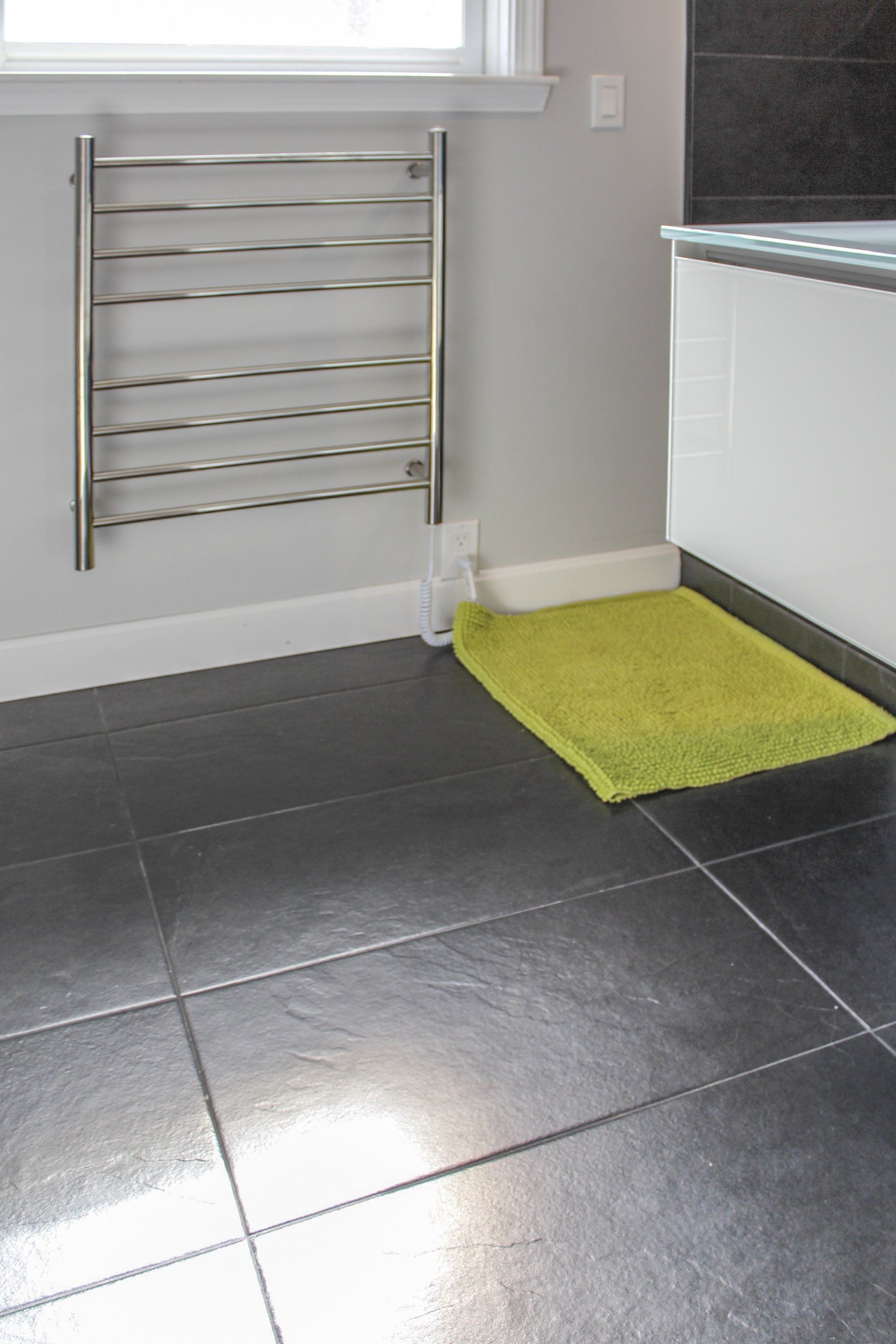 Bathroom corner with a chrome towel rack, white cabinet, dark tile floor, and a lime green bath mat.