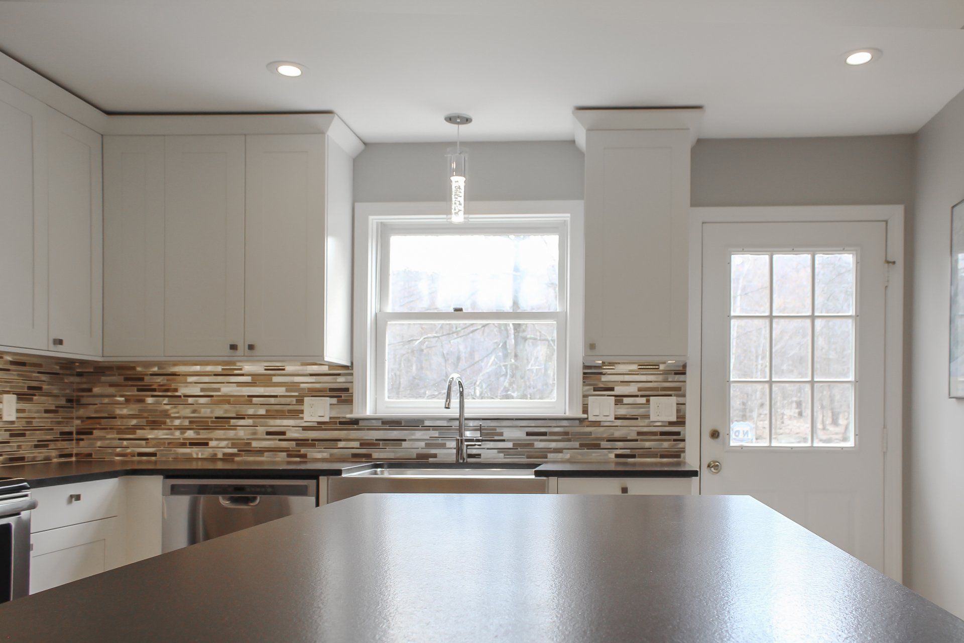Bright modern kitchen with white cabinets, mosaic backsplash, and a large island countertop.