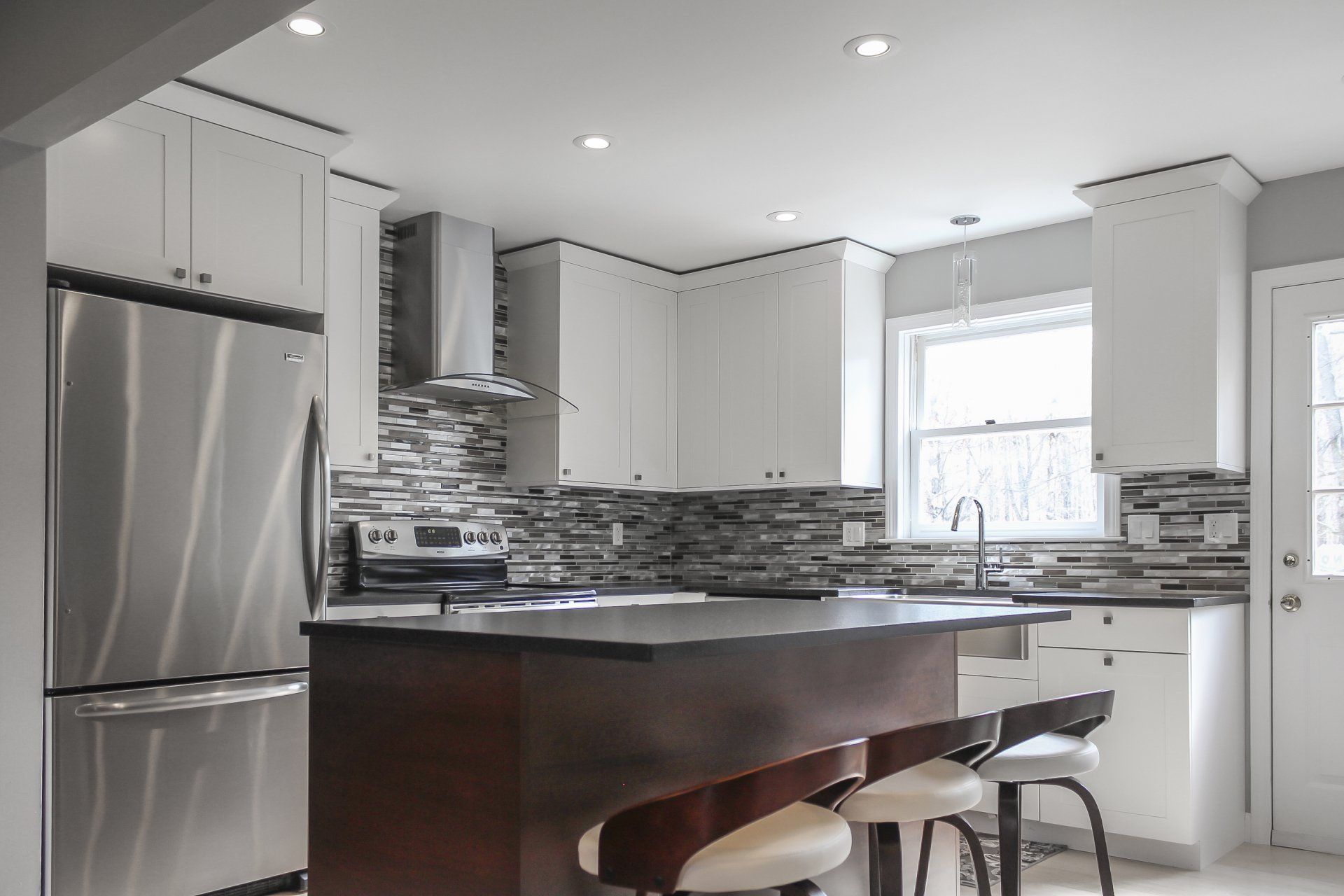 Modern white kitchen with stainless steel appliances, island, and mosaic tile backsplash