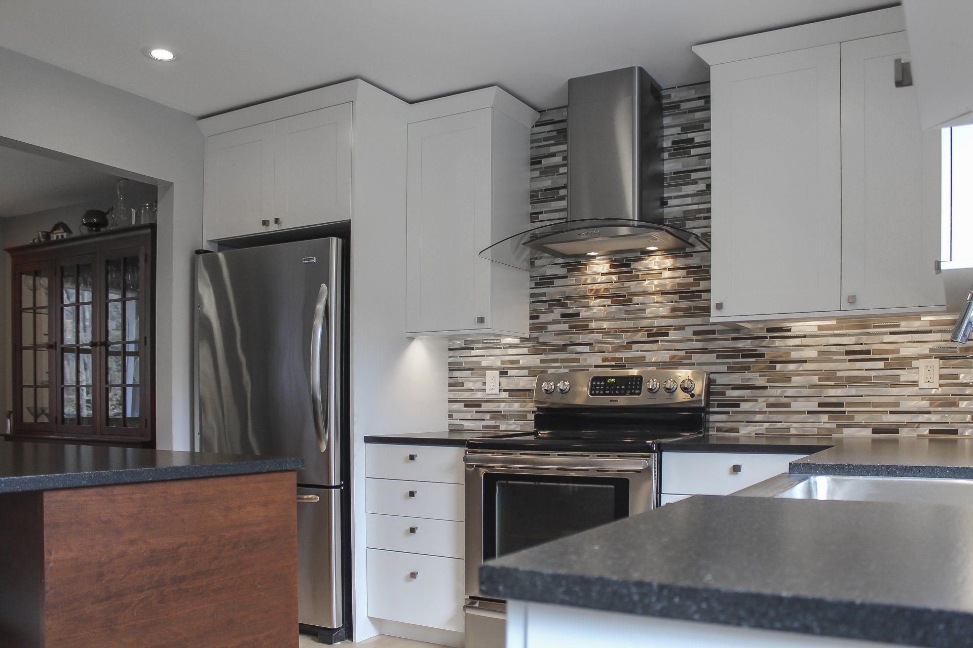 Modern kitchen with stainless steel appliances, white cabinets, mosaic backsplash, and dark countertops