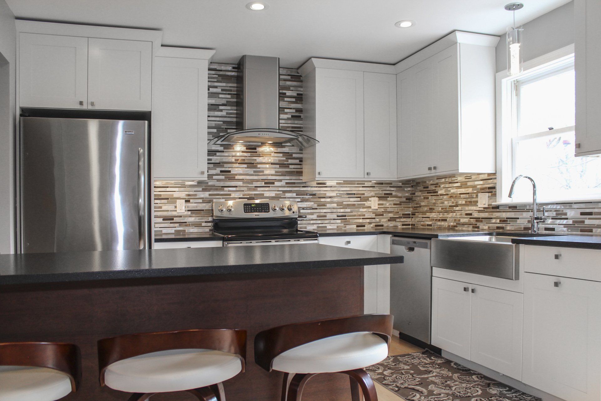 Modern kitchen with stainless steel fridge, dark island, white cabinets, and tiled backsplash