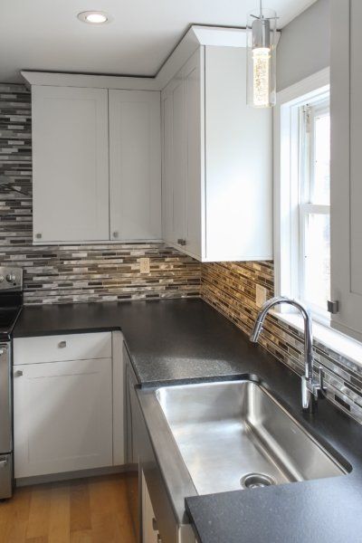 Modern kitchen with white cabinets, stainless-steel sink, dark countertops, and a tiled backsplash by a window