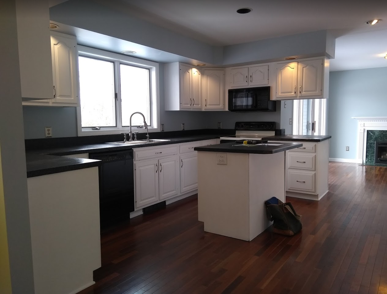 Modern kitchen with white cabinets, black countertops, island, stainless appliances, and dark hardwood floors