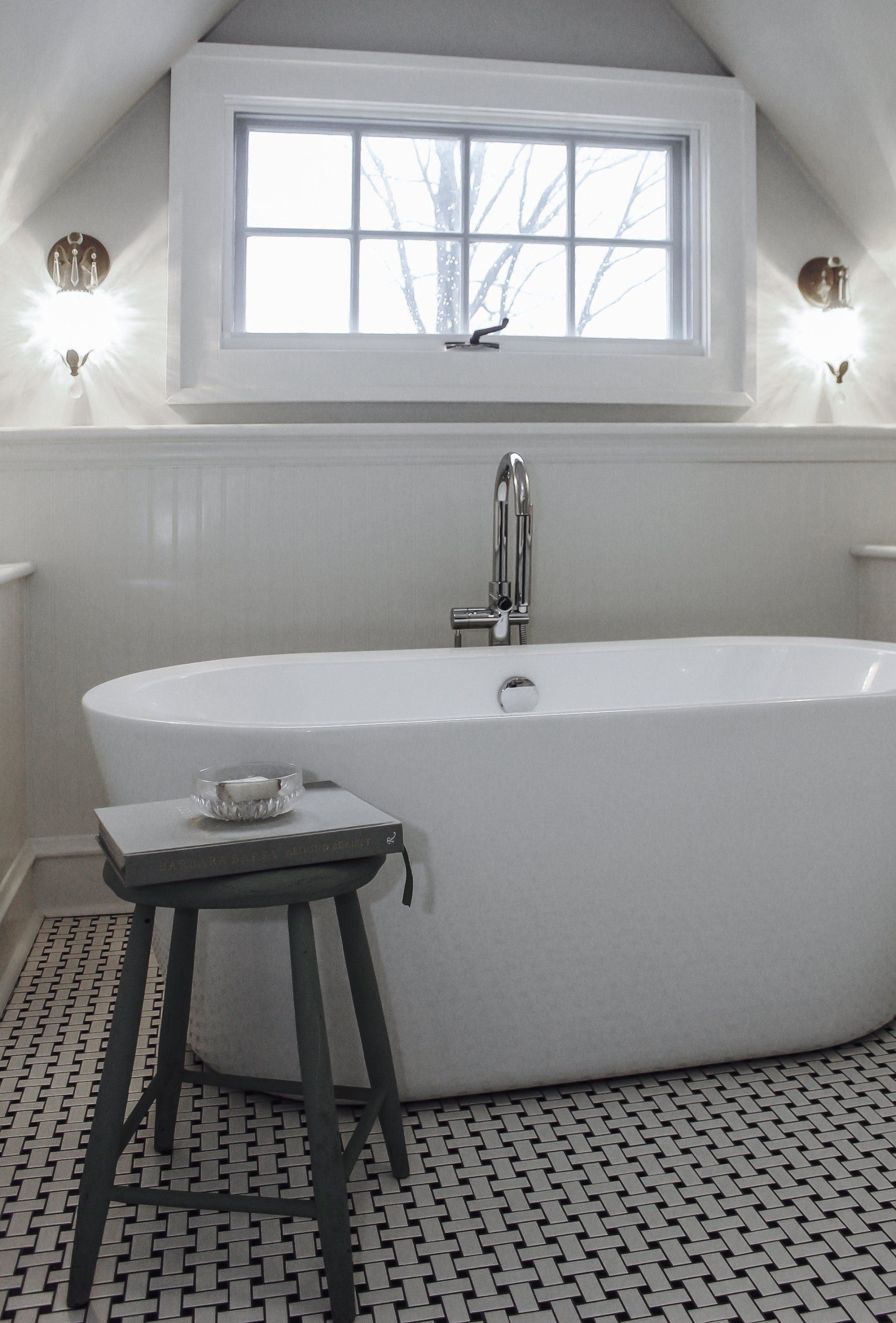 Bright white bathroom with a freestanding tub, small stool, and patterned black-and-white floor tiles.