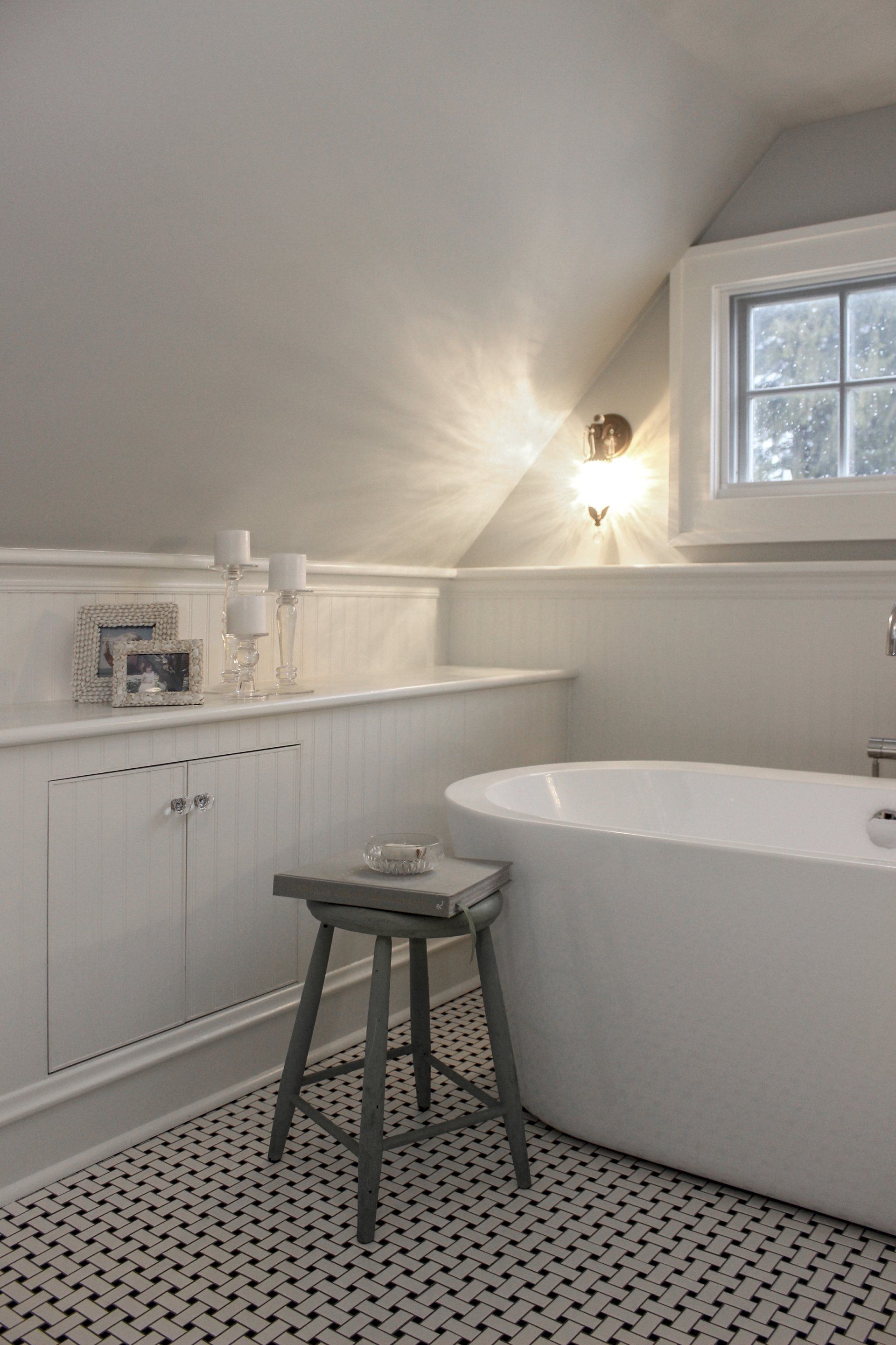 White bathroom with a clawfoot tub, small stool, wall sink, and patterned black-and-white tile floor.