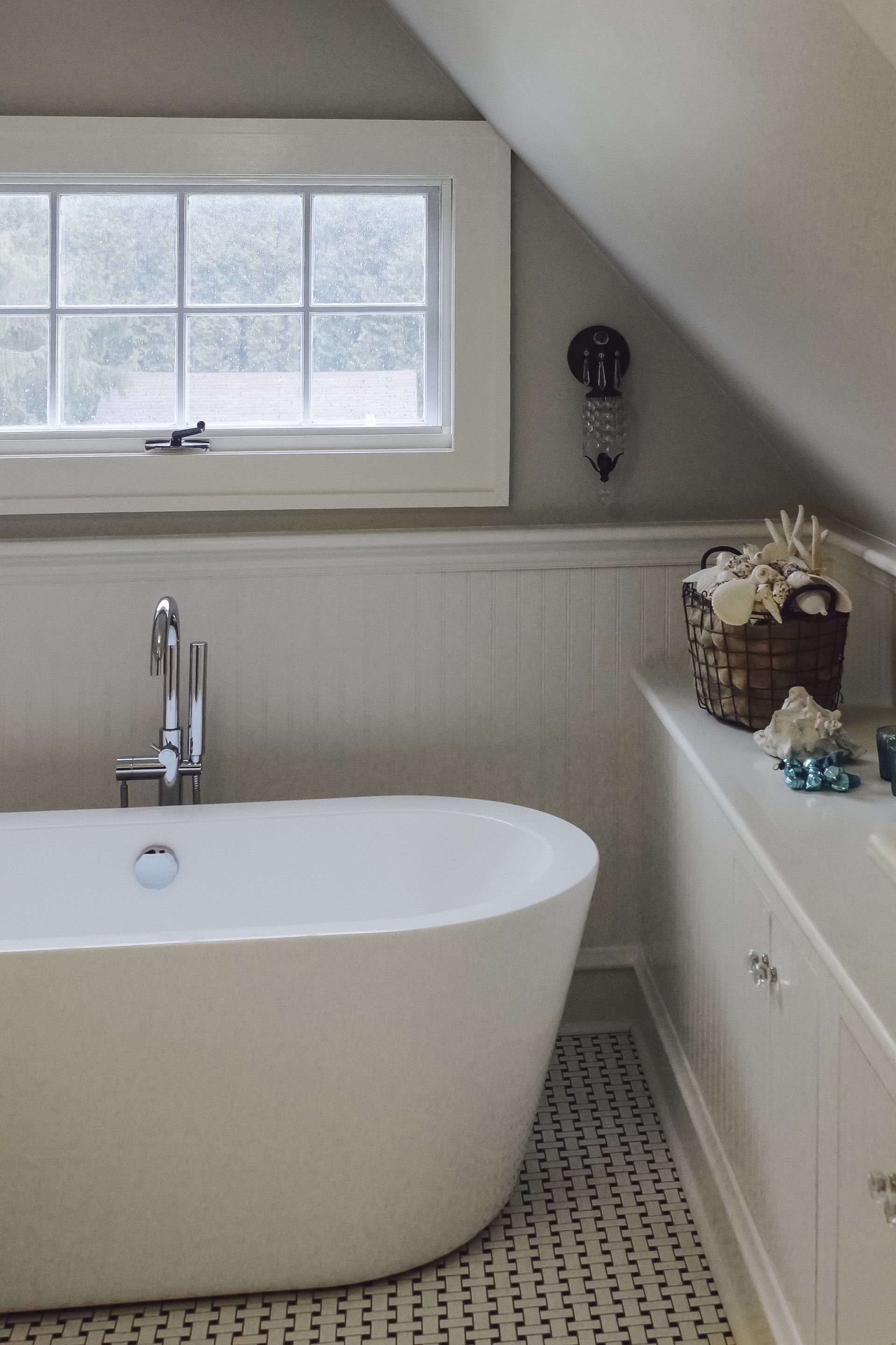Modern bathroom with freestanding tub, window, white wainscoting, and sloped ceiling