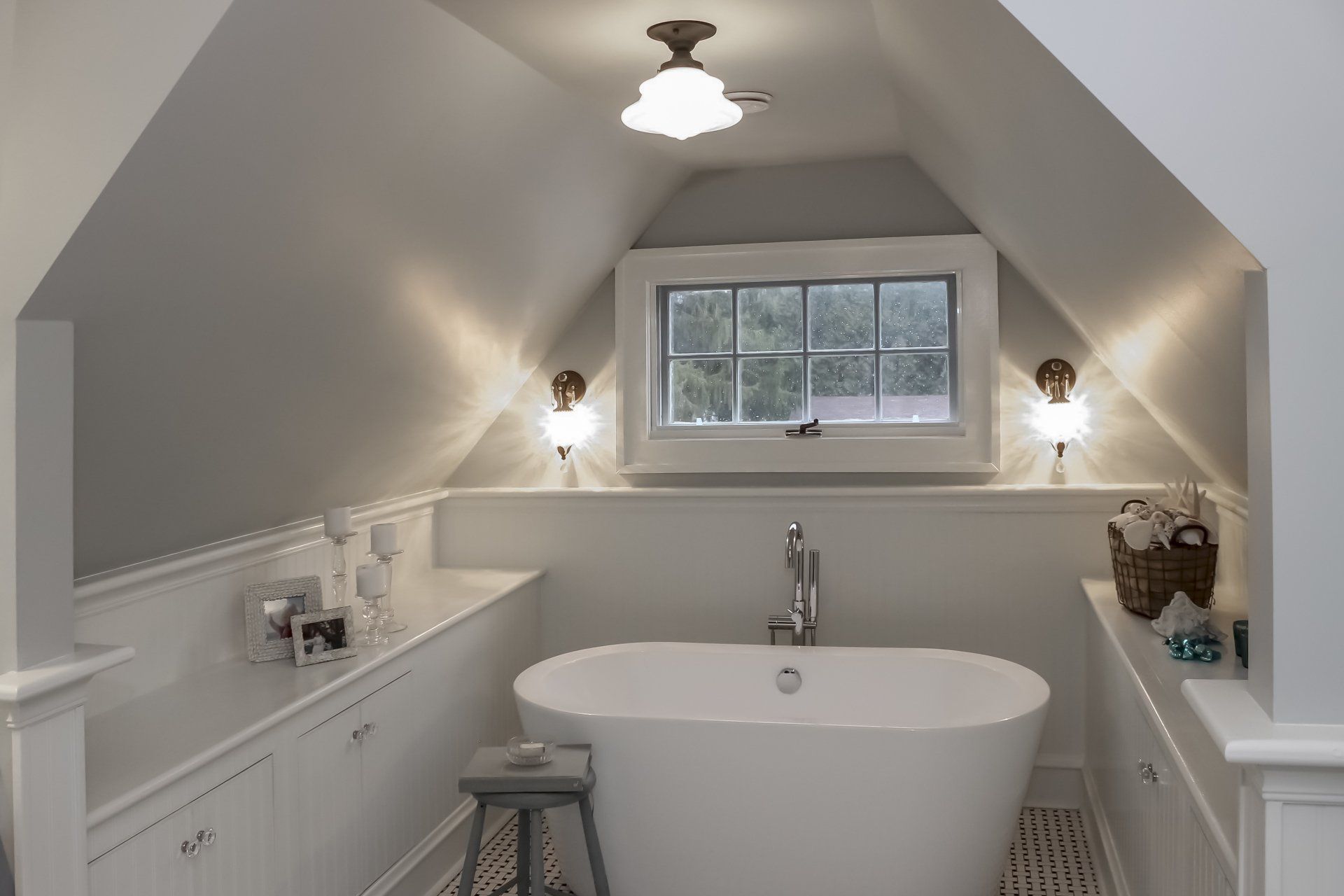 Bright attic bathroom with a freestanding tub, white walls, and two sconces by a window.