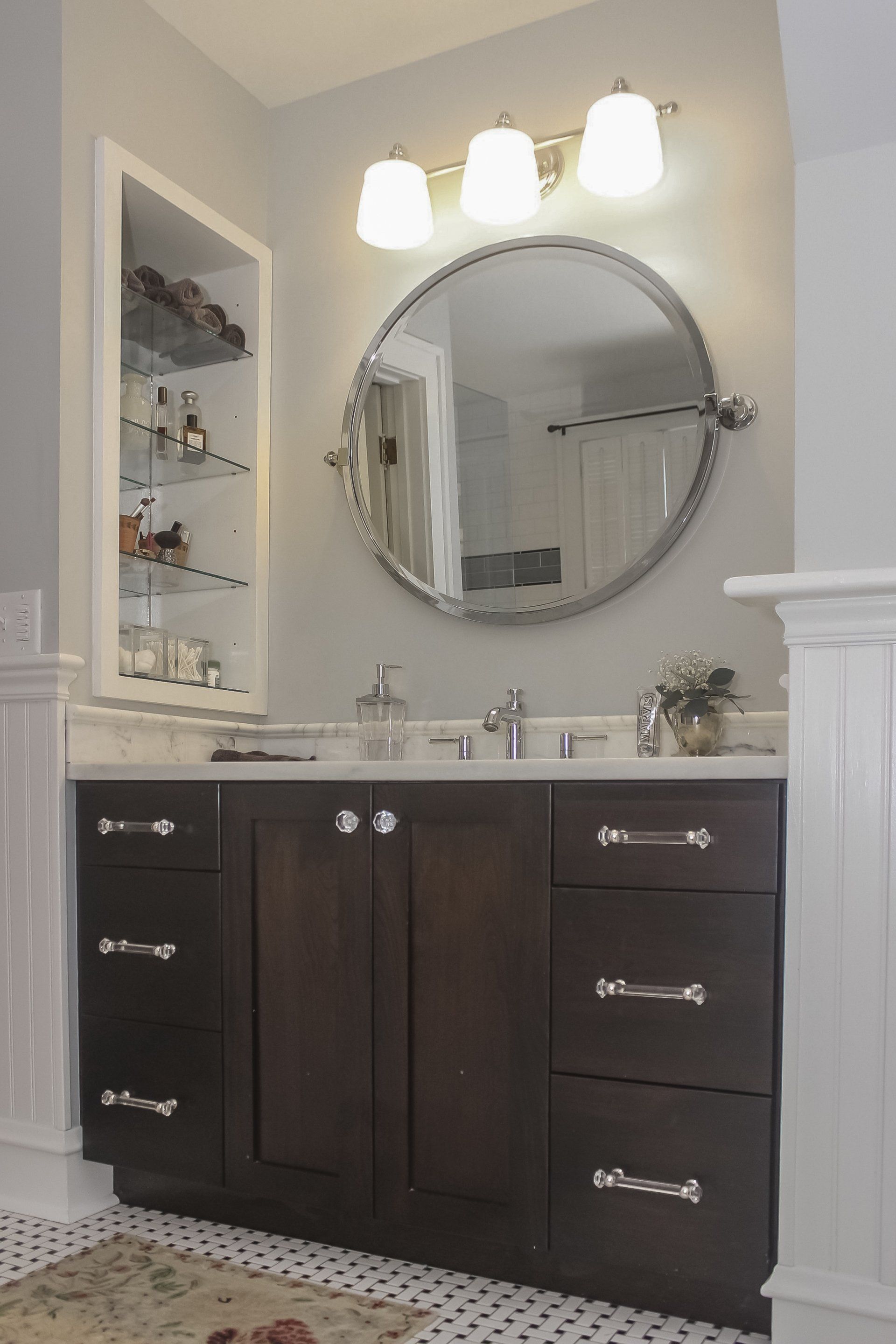 Dark wood bathroom vanity with sink, round mirror, and three wall lights in a tiled bathroom.