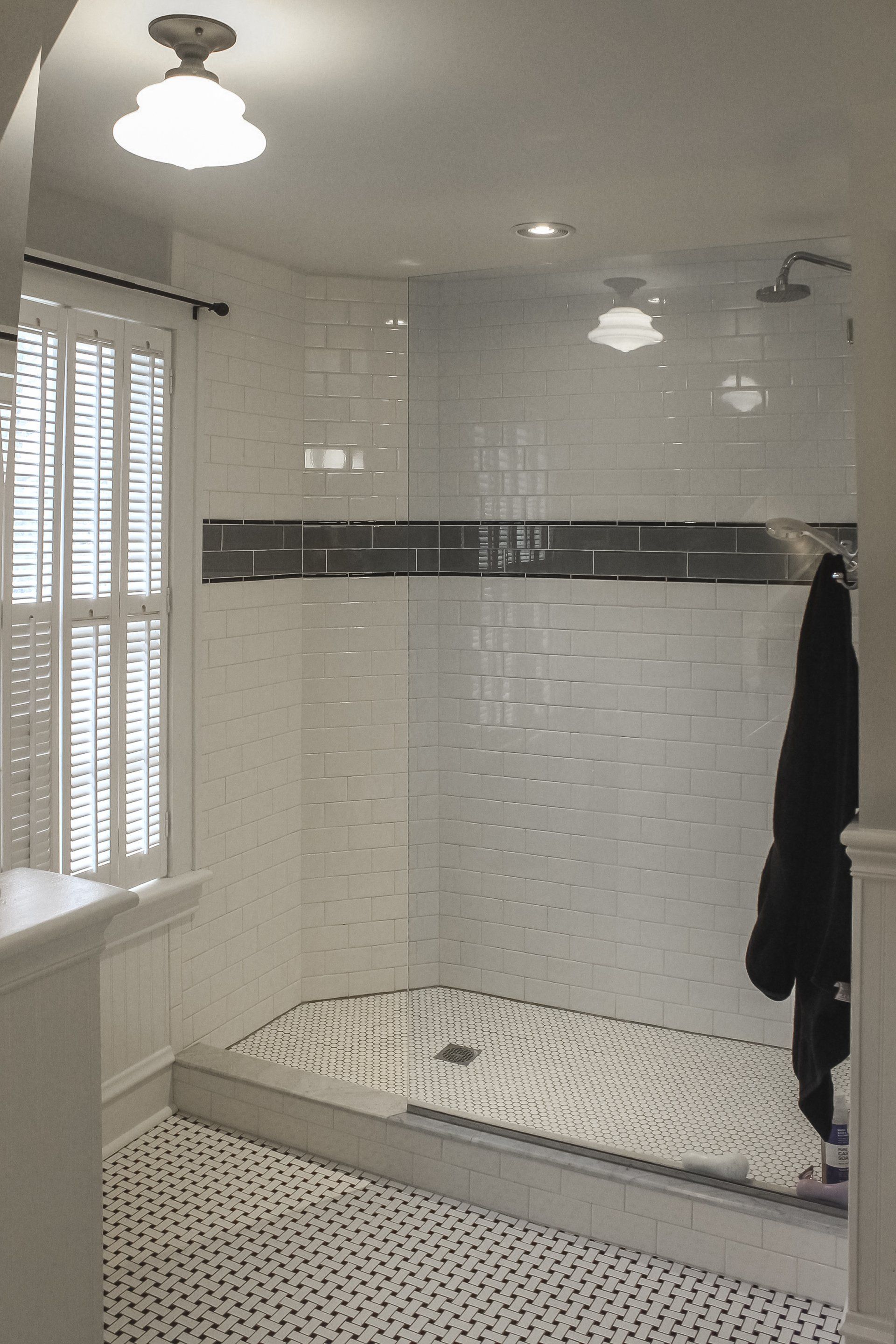 Tiled bathroom with a walk-in shower, white shower curtain, and black bathrobe hanging on the wall.