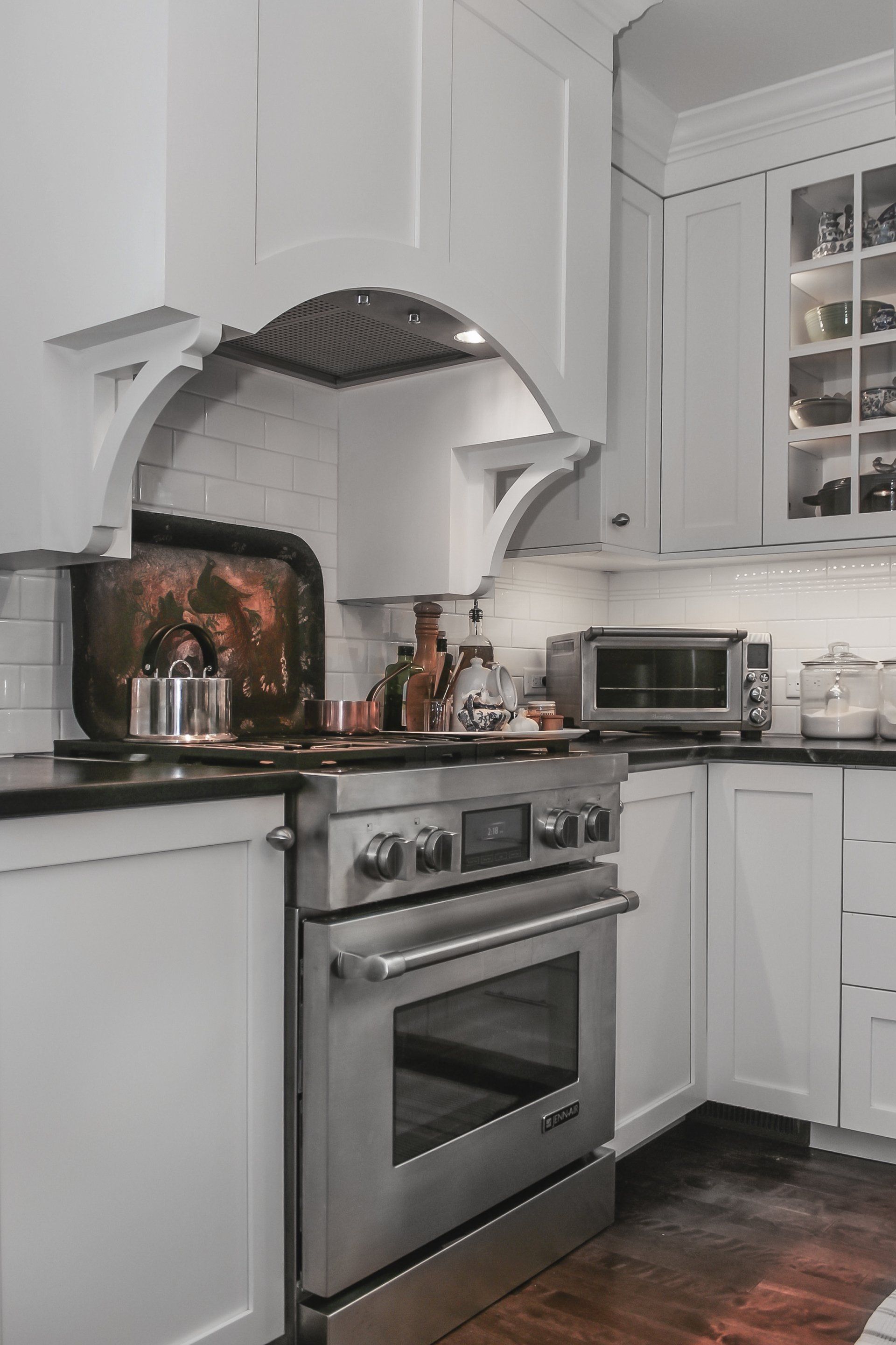 Bright white kitchen with stainless steel stove, arched hood, and dark wood floor