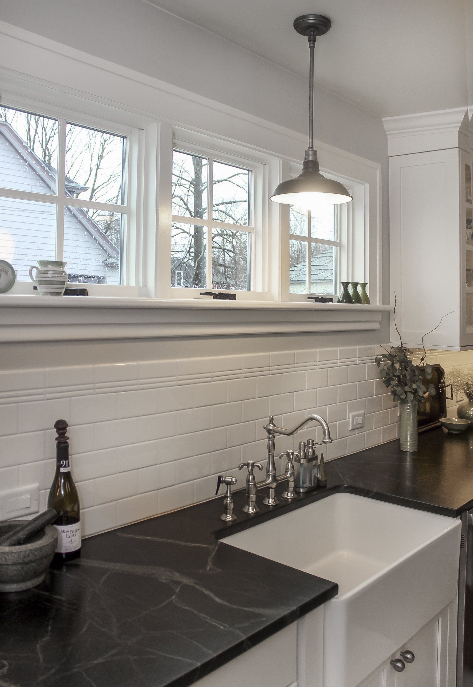 Bright white kitchen sink with dark countertop, windows, and pendant light above a brick backsplash