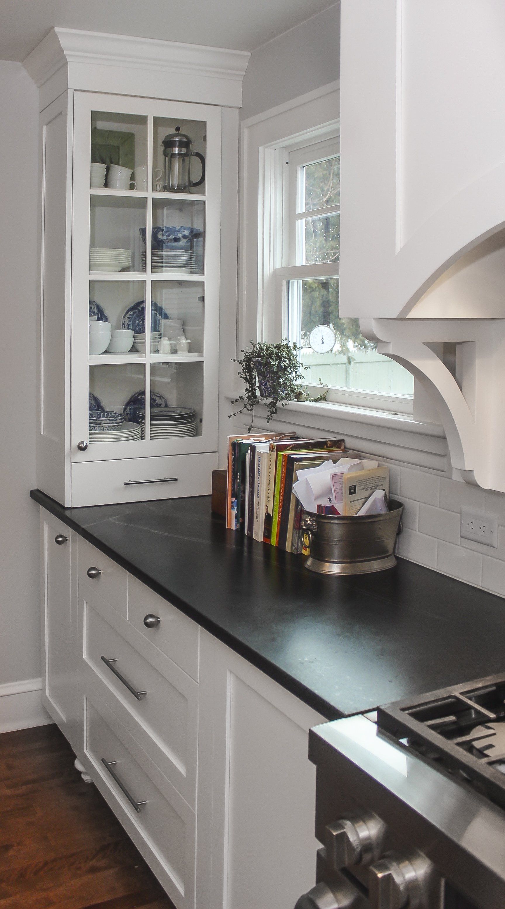 Bright white kitchen with black countertop, window, and glass cabinet displaying dishes.