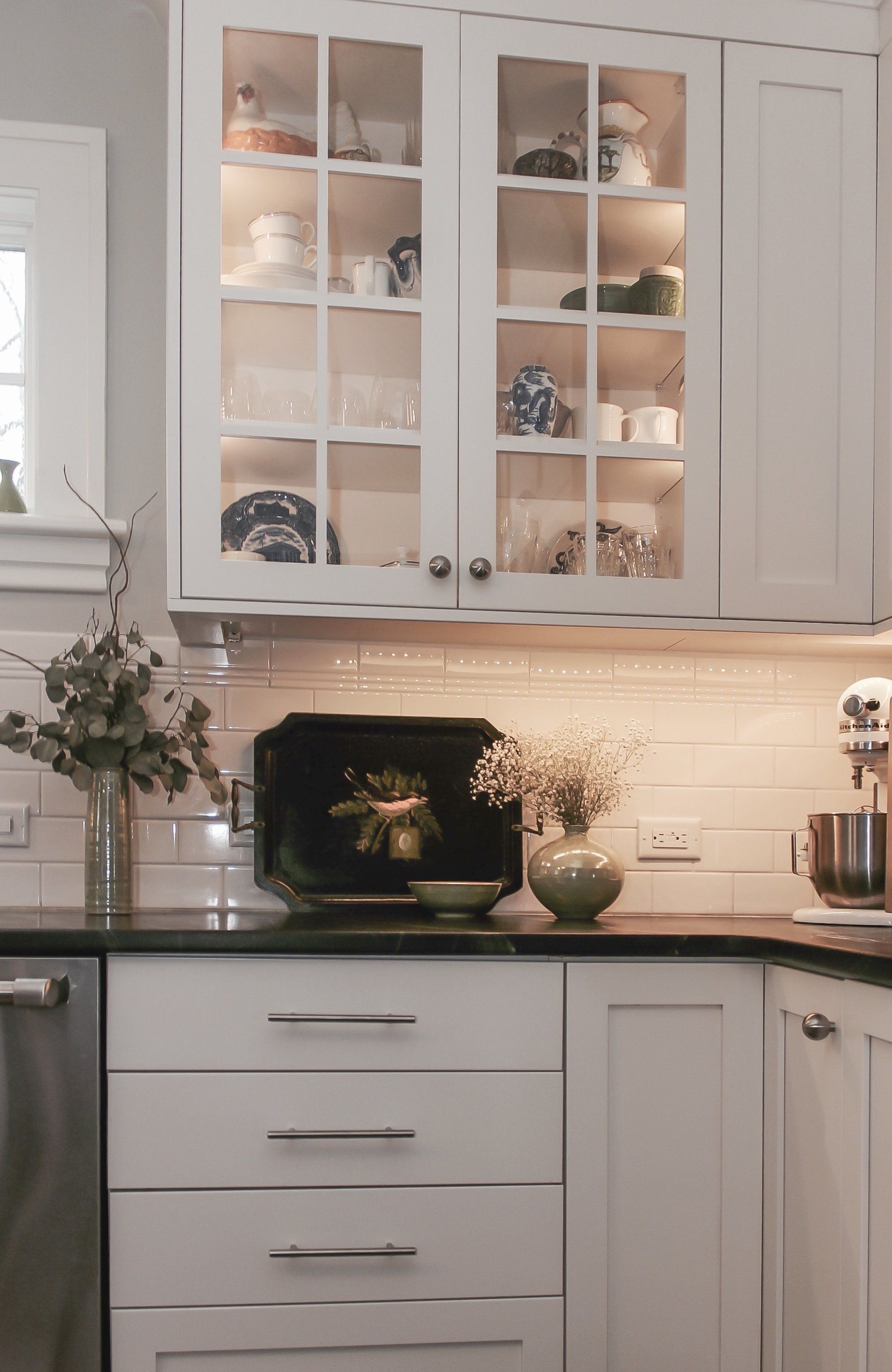 White kitchen with glass-front cabinets, dark countertop, black stove, and warm under-cabinet lighting.