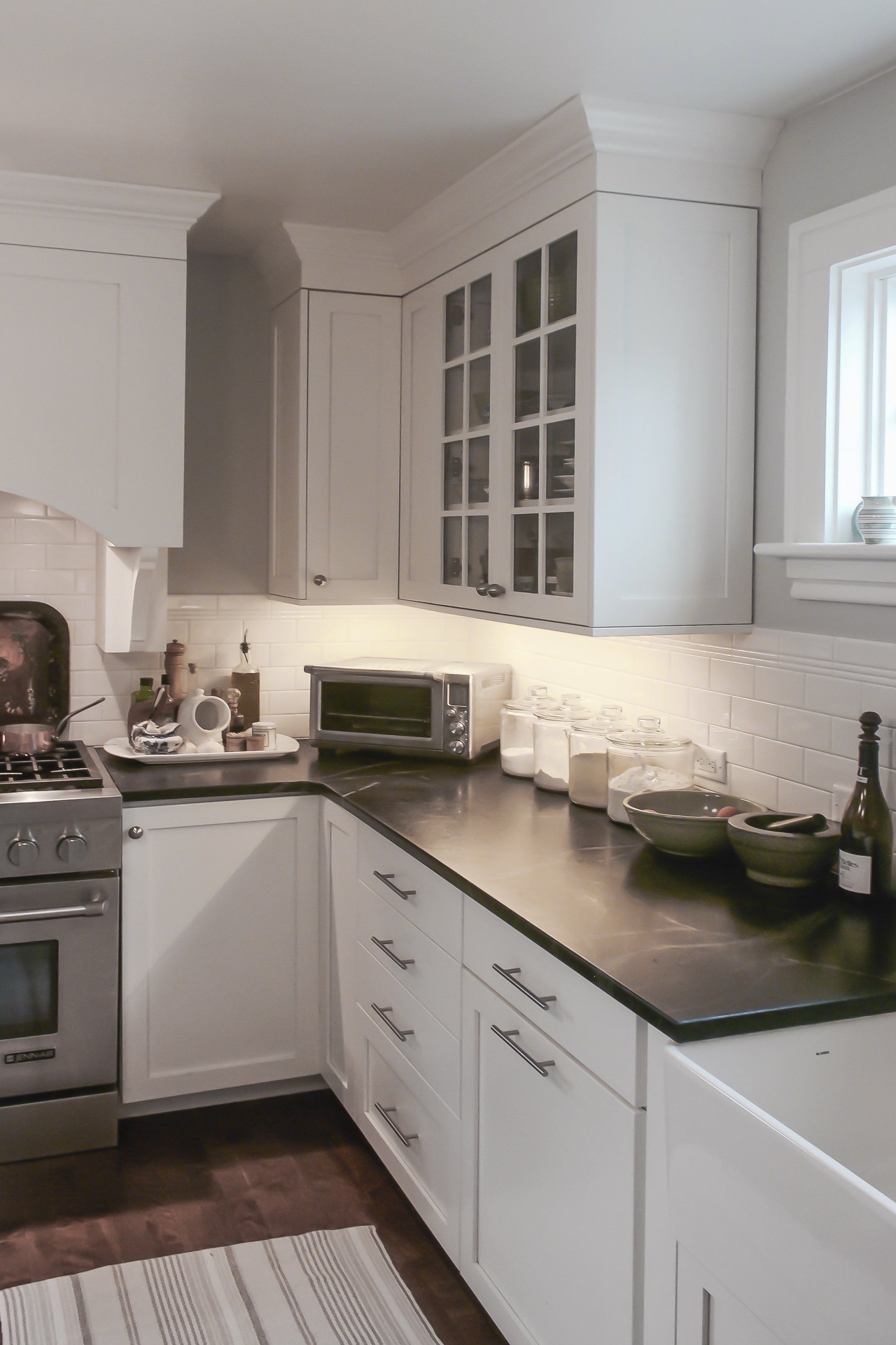 Bright white kitchen with black countertops, stove, cabinets, and a small window above the sink.