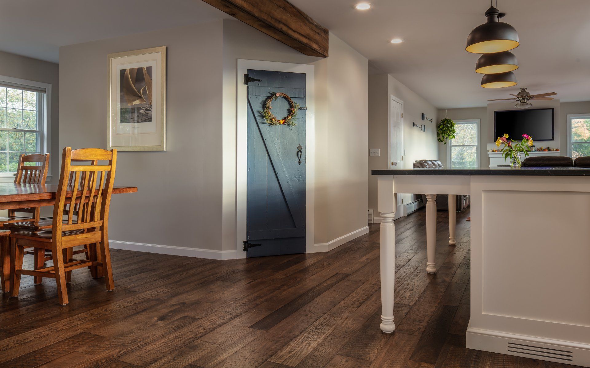 Open dining and kitchen area with wood floors, dark island, dining table, and a blue door with wreath.