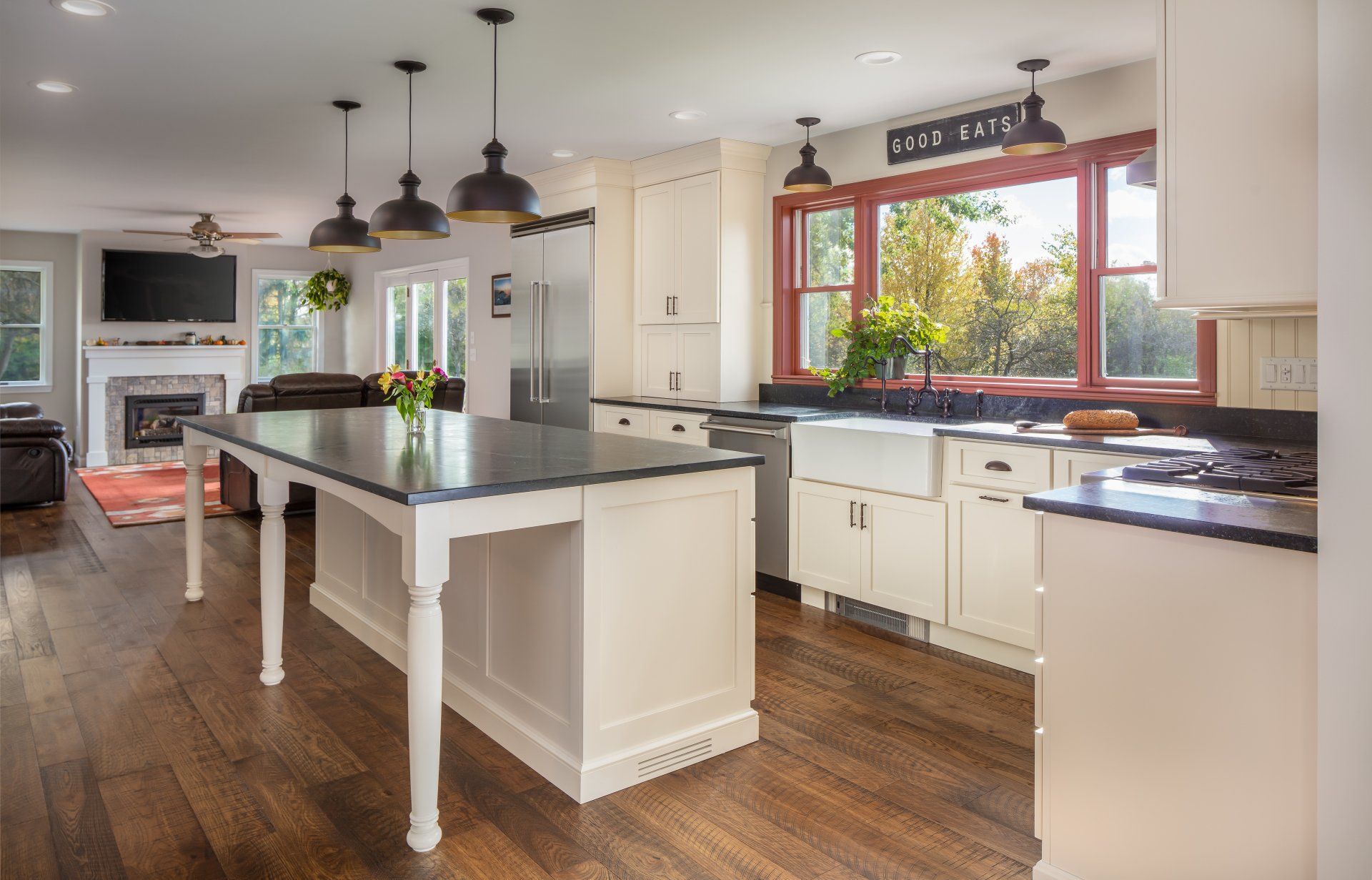 Bright modern kitchen with white cabinets, dark island, wood floors, and large window over the sink.