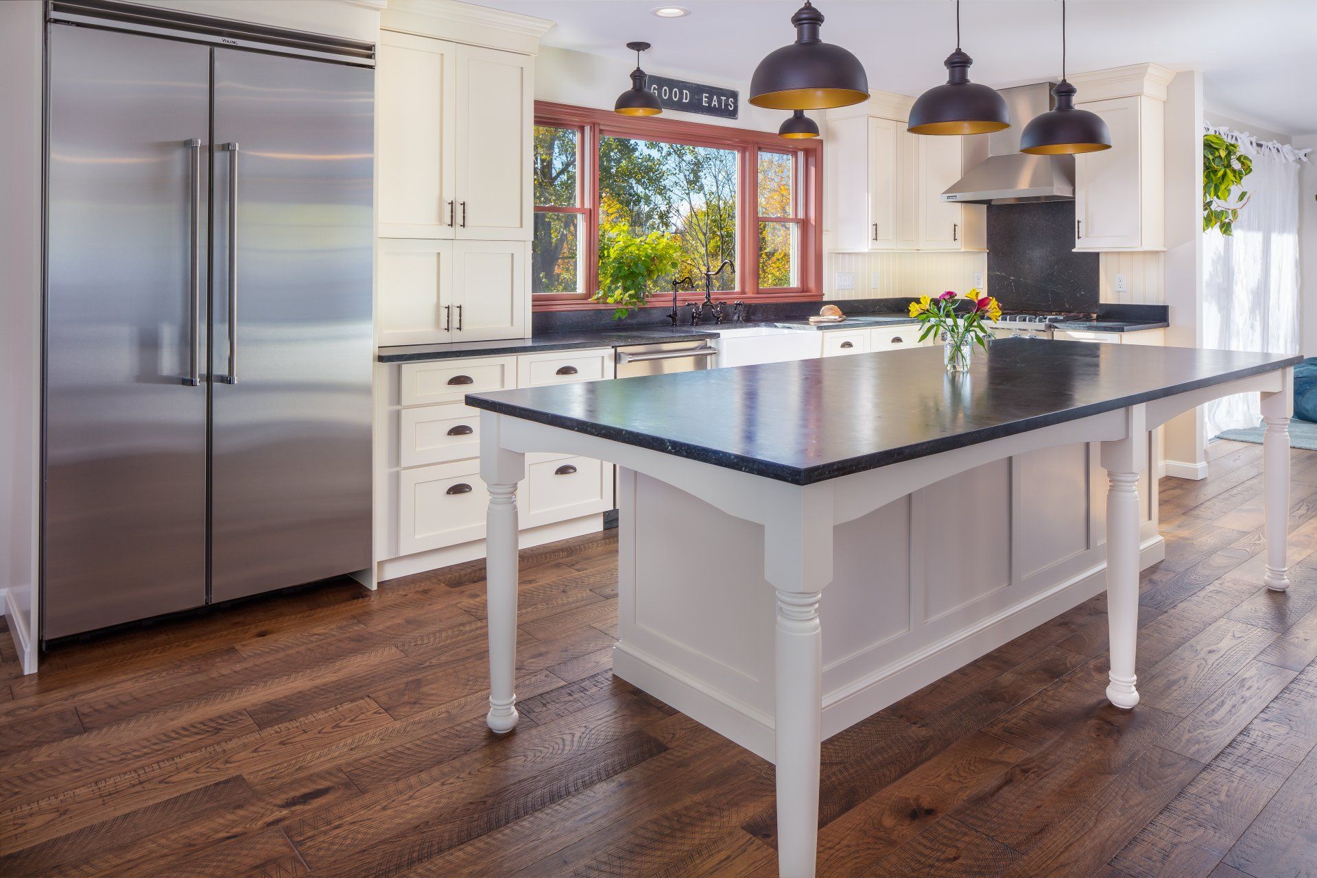 Bright modern kitchen with white cabinets, black island countertop, stainless fridge, and pendant lights