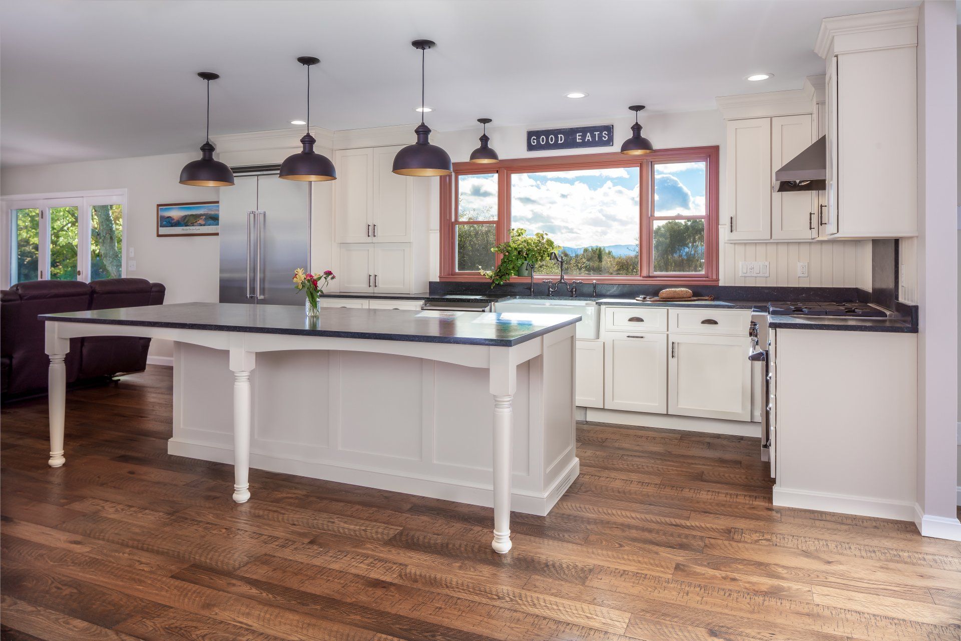 Bright modern kitchen with white cabinets, island, wood floors, and pendant lights.