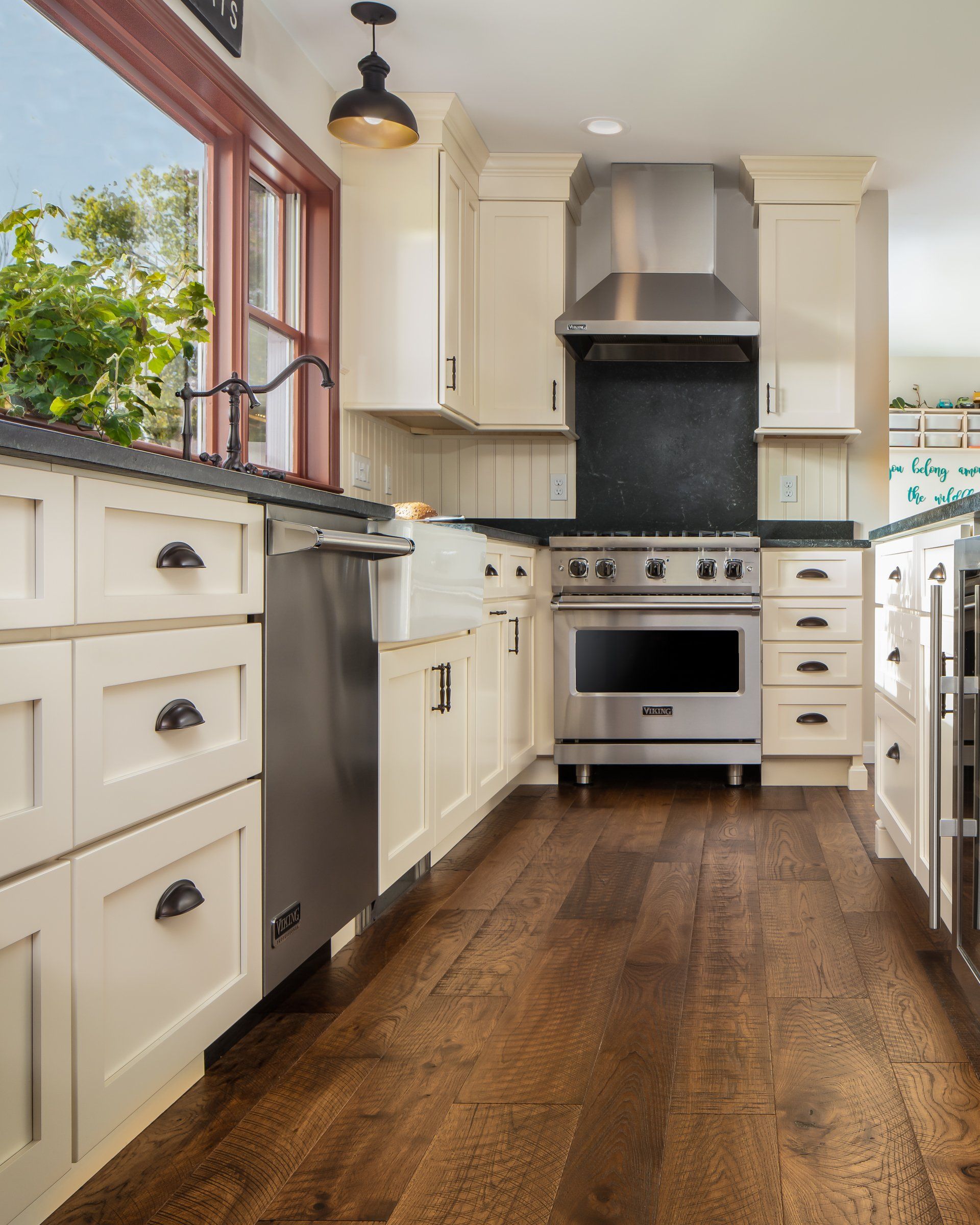 Bright kitchen with white cabinets, stainless-steel stove, and wooden floor beside a window
