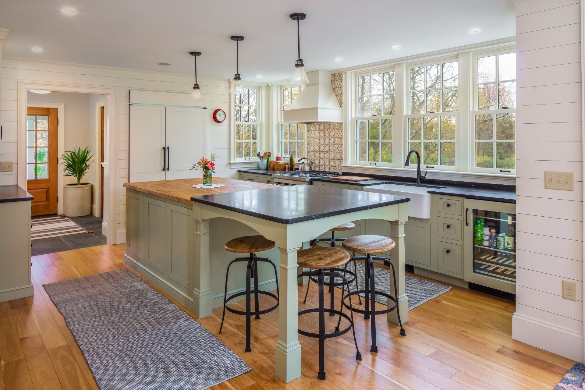 Bright kitchen with a large island, stools, pendant lights, and sunlit windows.