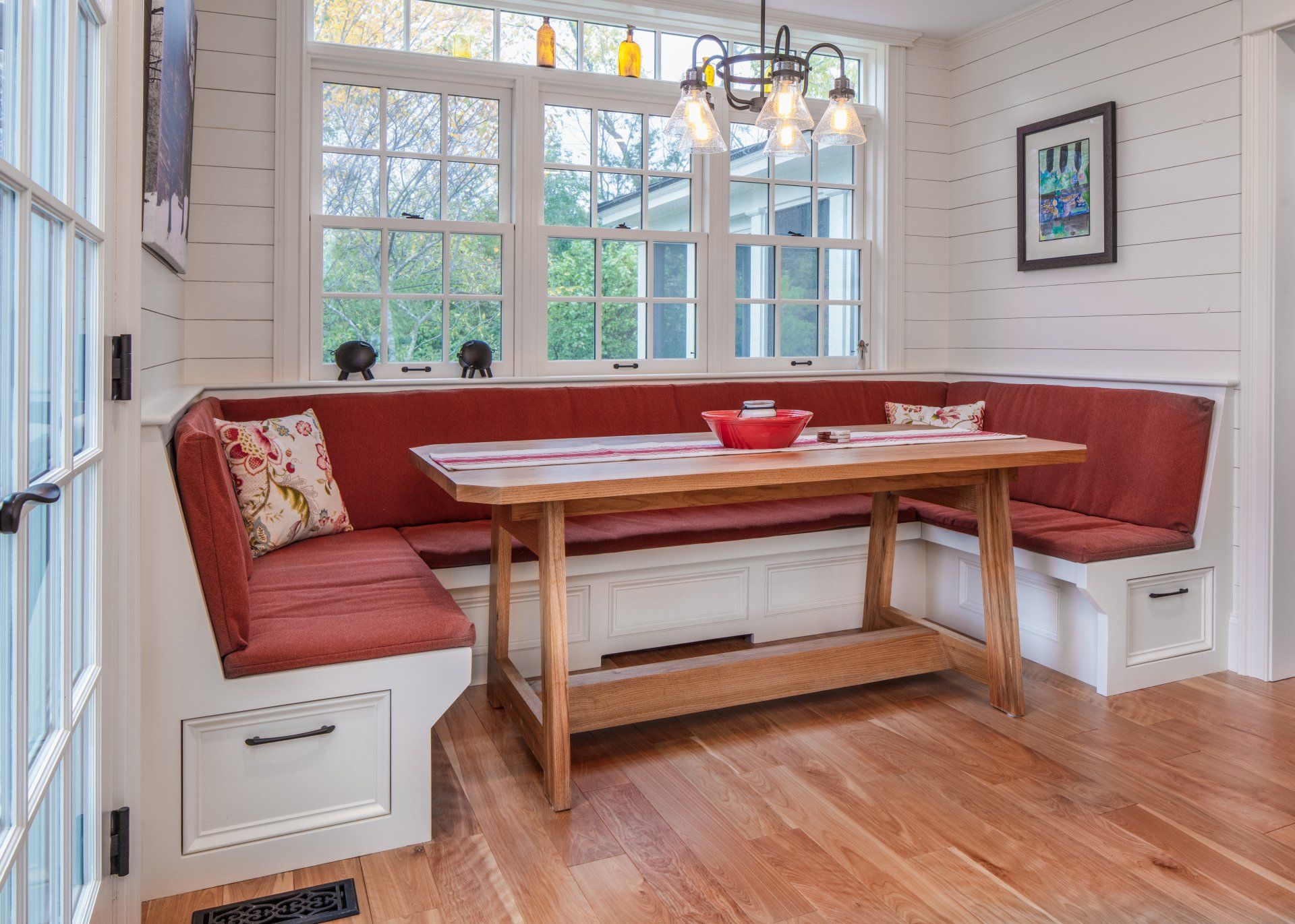 Cozy breakfast nook with red bench seating, wood table, and bright windows